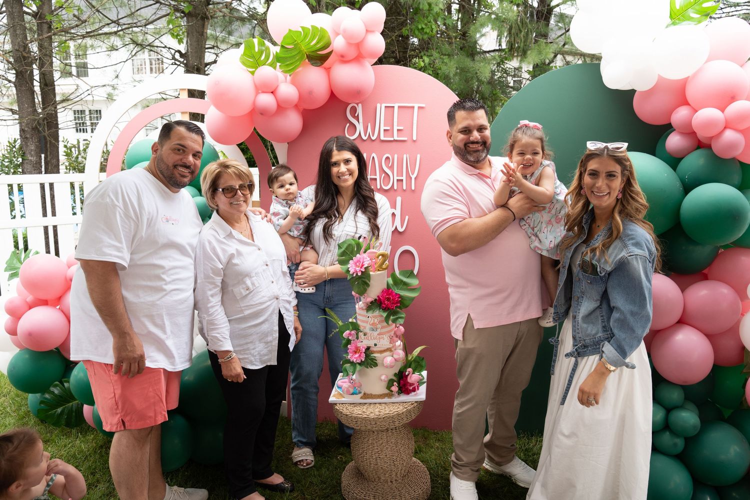 Party outdoor gathering with balloon arches and decorative backdrops in pink and green.