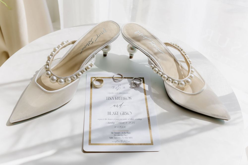 Elegant white bridal shoes with pearl details arranged with wedding invitation.