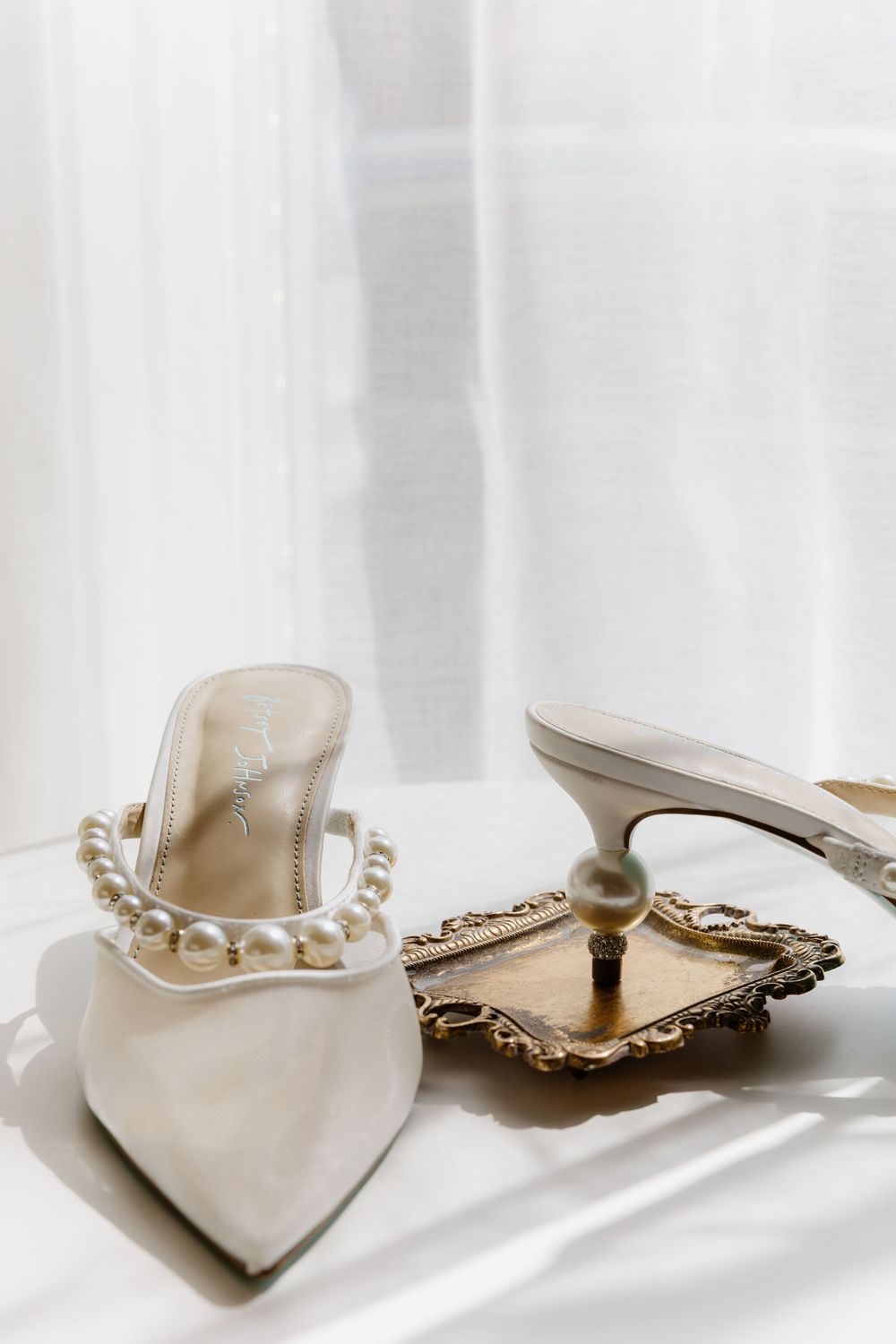 Elegant bridal shoes with pearl details displayed against white fabric in natural light.