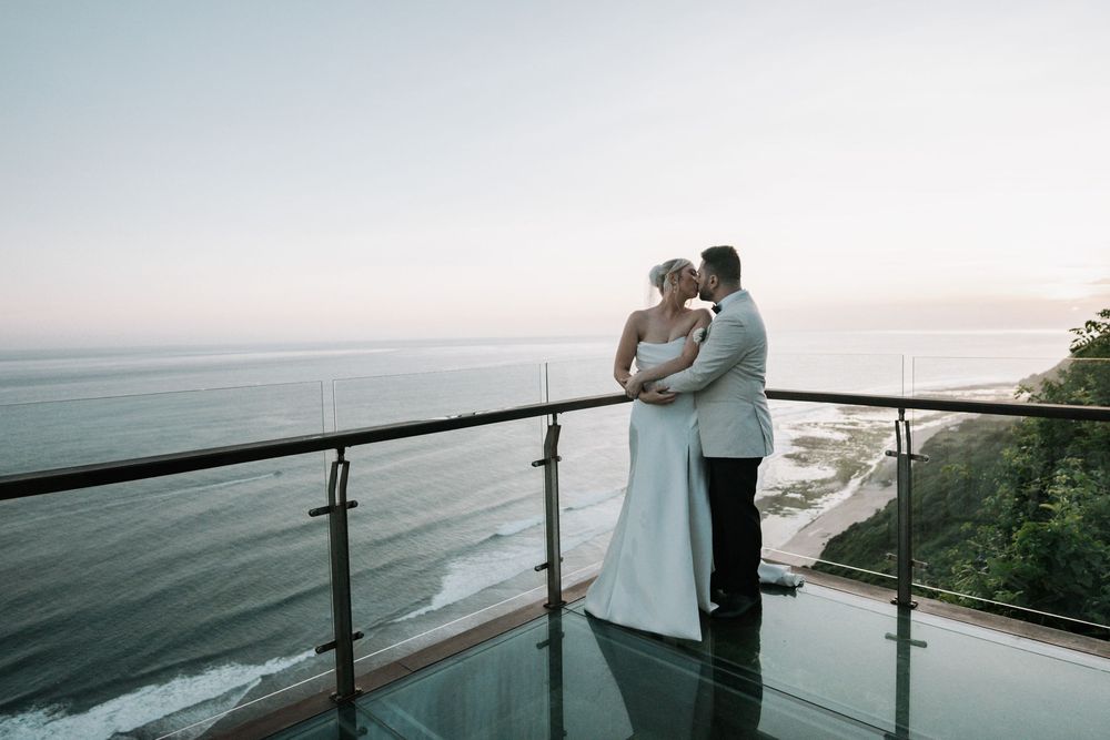Romantic couple embraces while overlooking scenic ocean views from a deck railing at sunset.