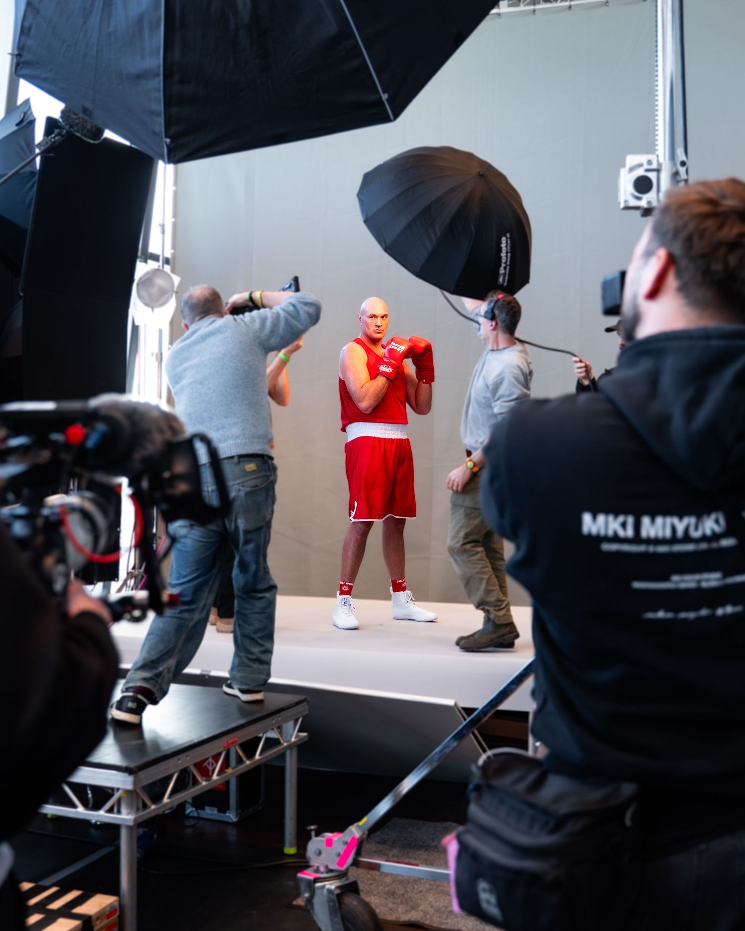 Behind-the-scenes photo shoot setup in a studio with lighting equipment and photographers capturing a model in red.