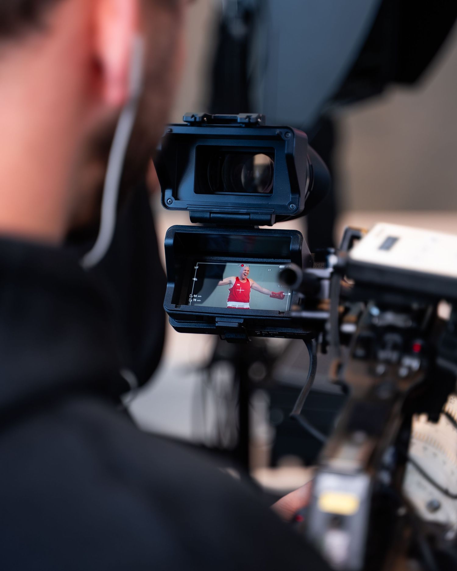A small red figure is visible through a camera viewfinder while filming video equipment in a dark setting.