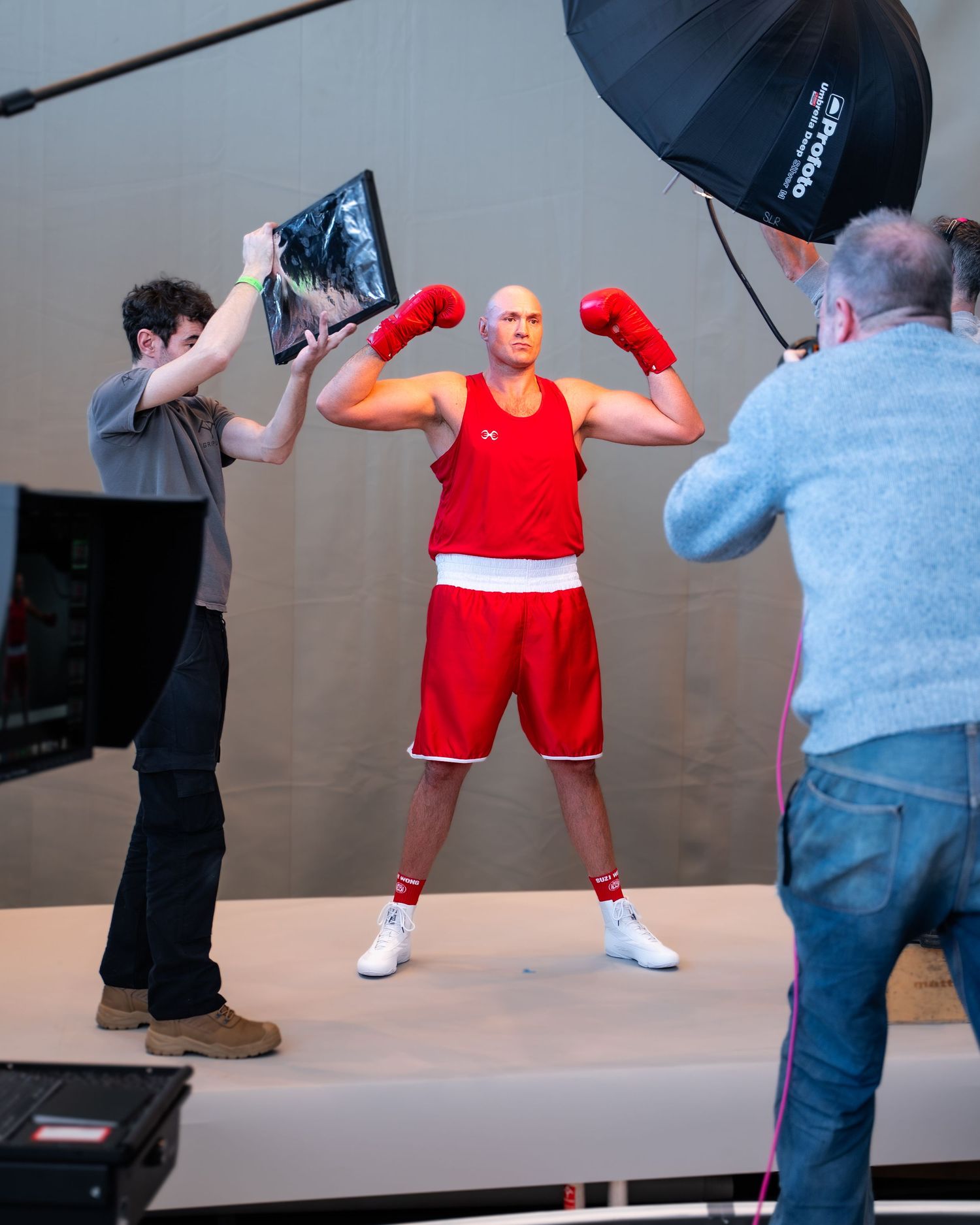 Behind-the-scenes photo shoot showing a boxer in red uniform posing while photographers capture the action.