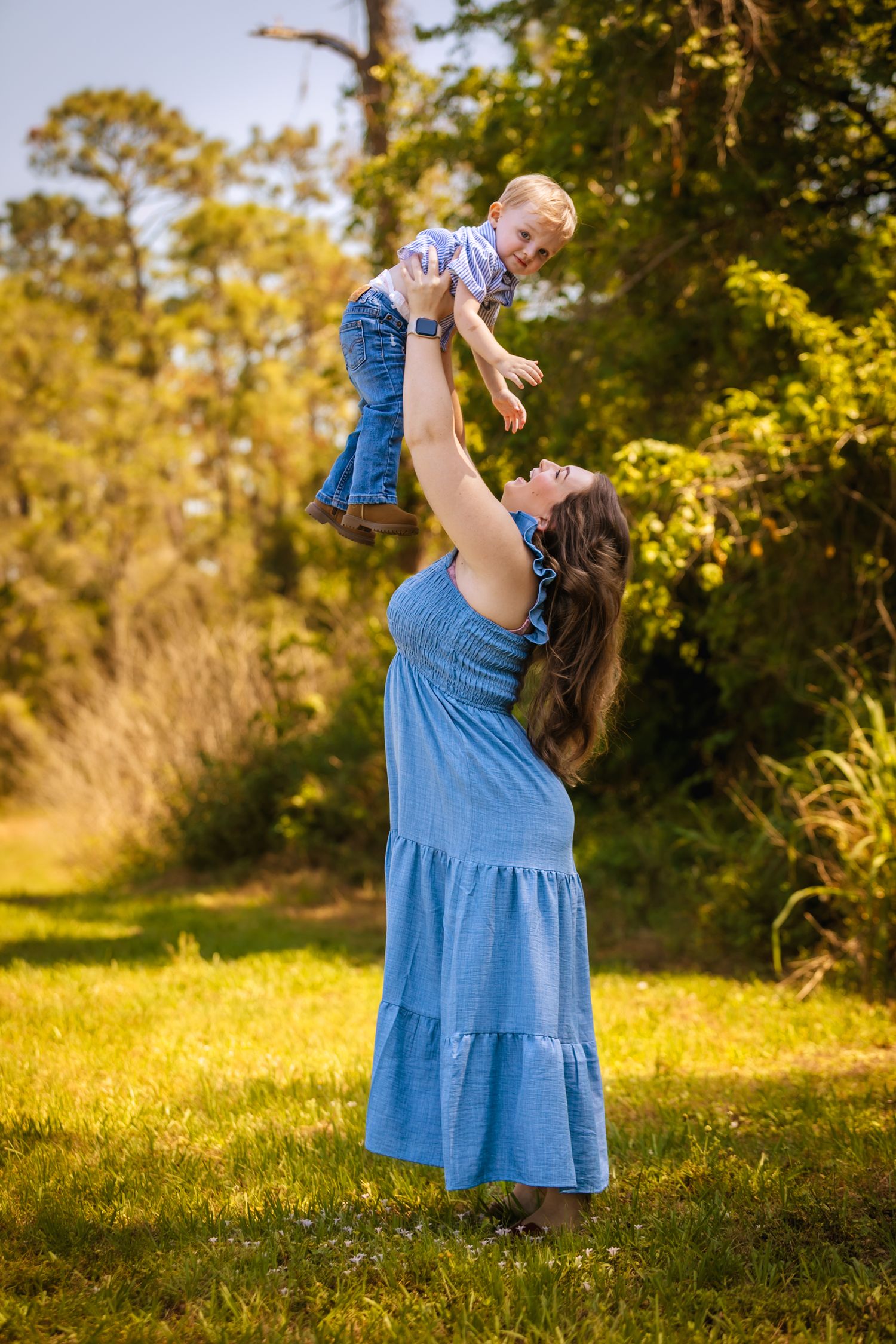 A playful outdoor moment in blue attire and denim as a child is lifted high into the air on a sunny day in nature.