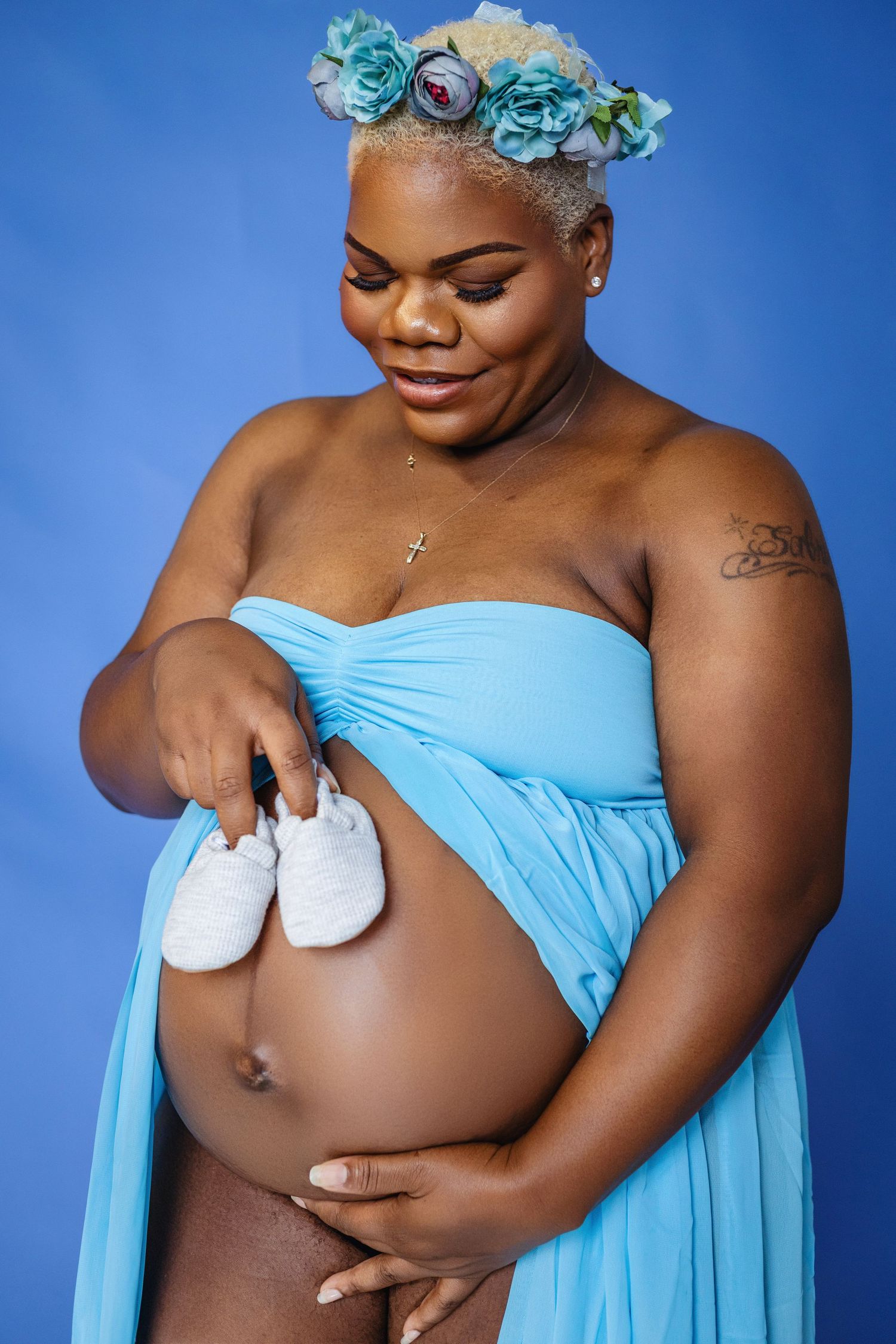 Maternity photoshoot with subject in blue dress and floral crown against blue background.