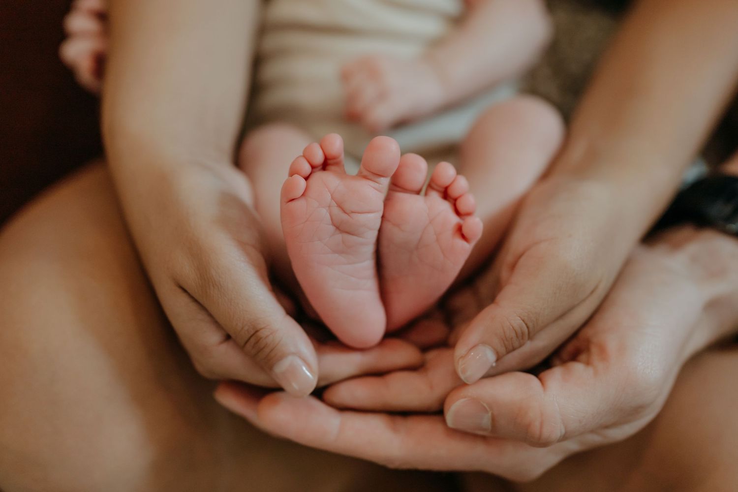 Small baby feet being gently held in adult hands showing tender parental care and bonding.