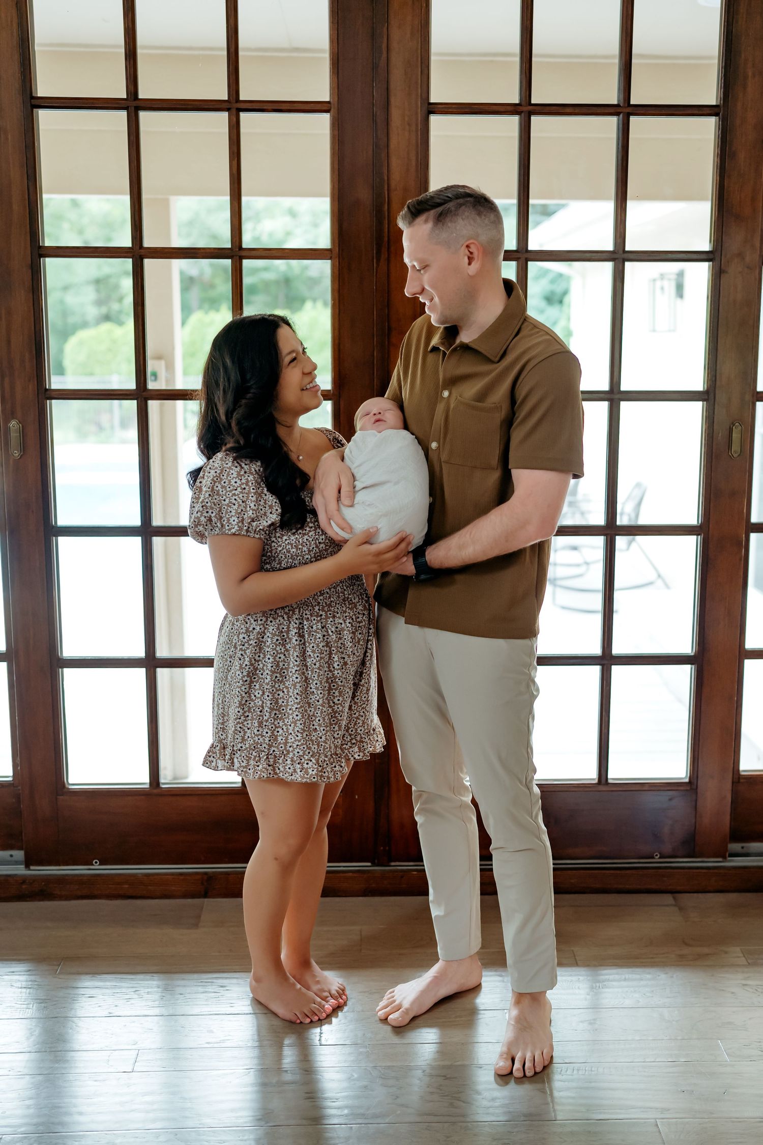 A couple embraces while standing barefoot in a bright studio space with wooden floors and walls.