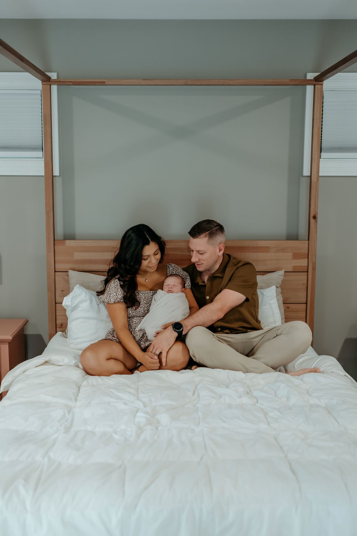 A couple rests together on white bedding in a cozy bedroom setting with wooden accents.