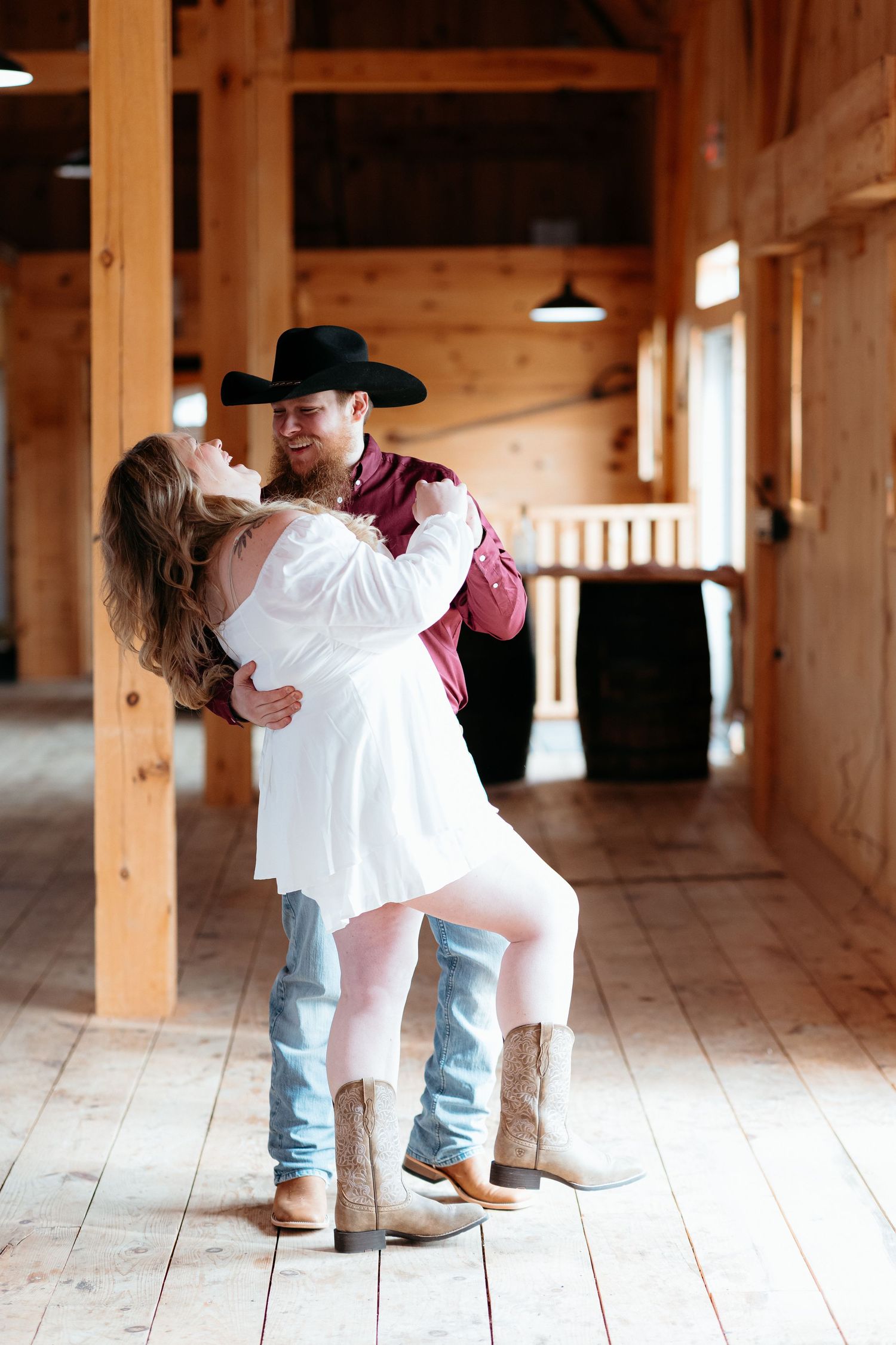 Romantic couple in western attire dancing in rustic barn setting with wooden beams. Serendipity Wedding Barn. Western Engagement session.