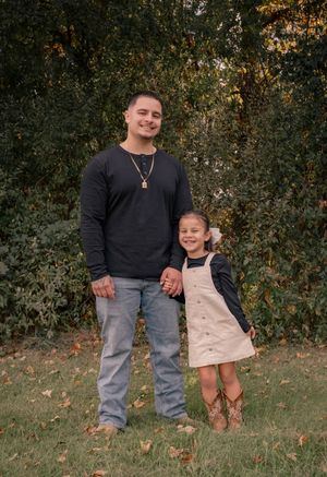 A parent and child holding hands outdoors in autumn, wearing casual clothing against a backdrop of fall foliage.