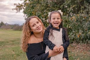Mother and child laughing and hugging while playing outdoors in an autumn setting with trees and fields in background.