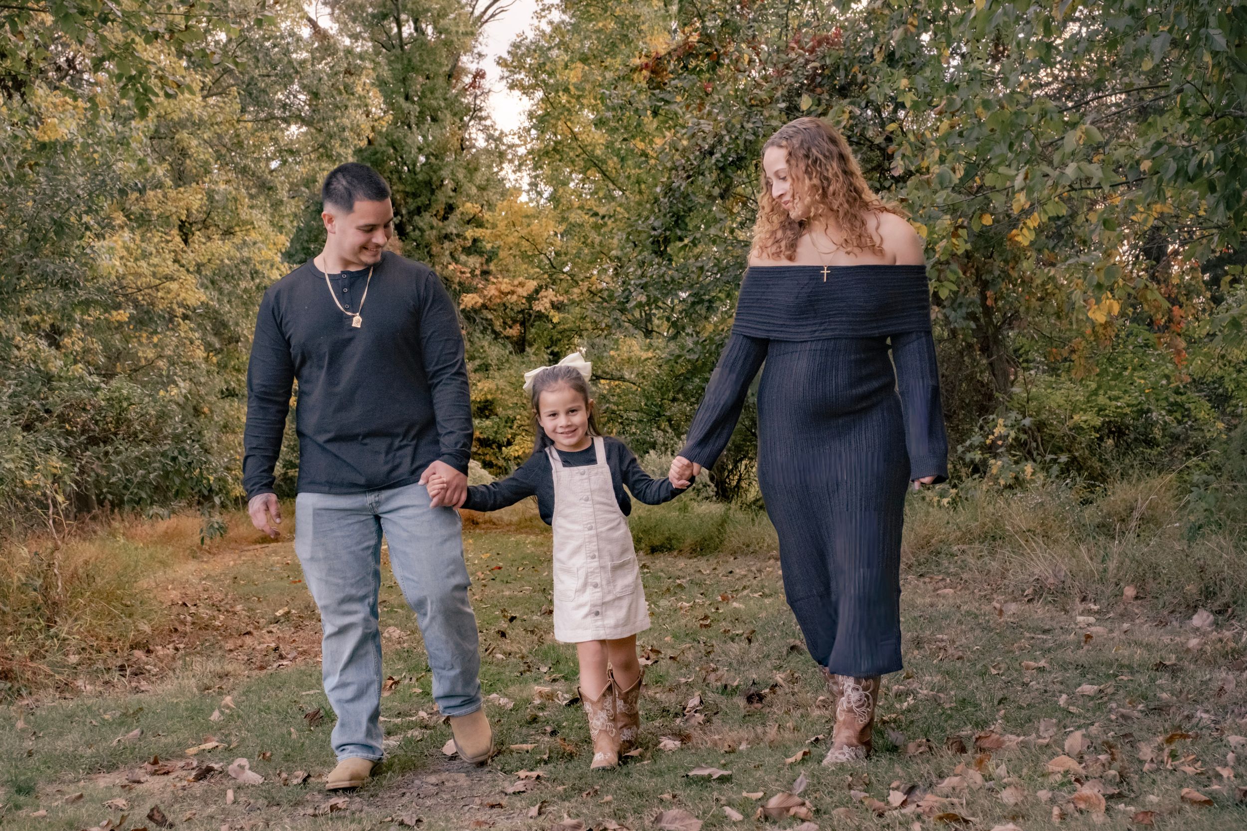 A group of people walking together on fallen autumn leaves in a wooded outdoor setting during a photo session.