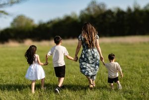 A family walking hand in hand through a grassy field on a sunny day.