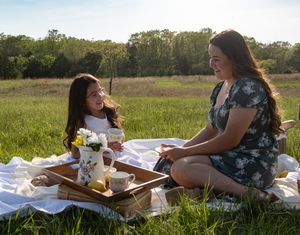 Two people enjoying a picnic on a blanket in a sunny field with flowers.