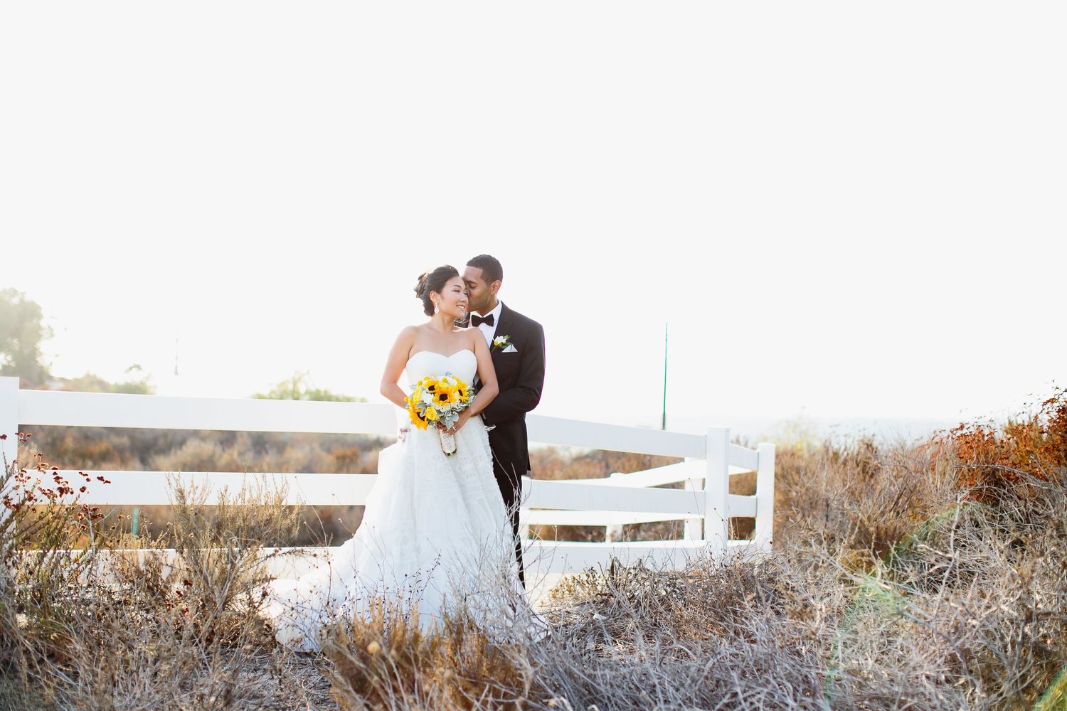 Wedding photo session in rustic field with white fence and autumn colors.