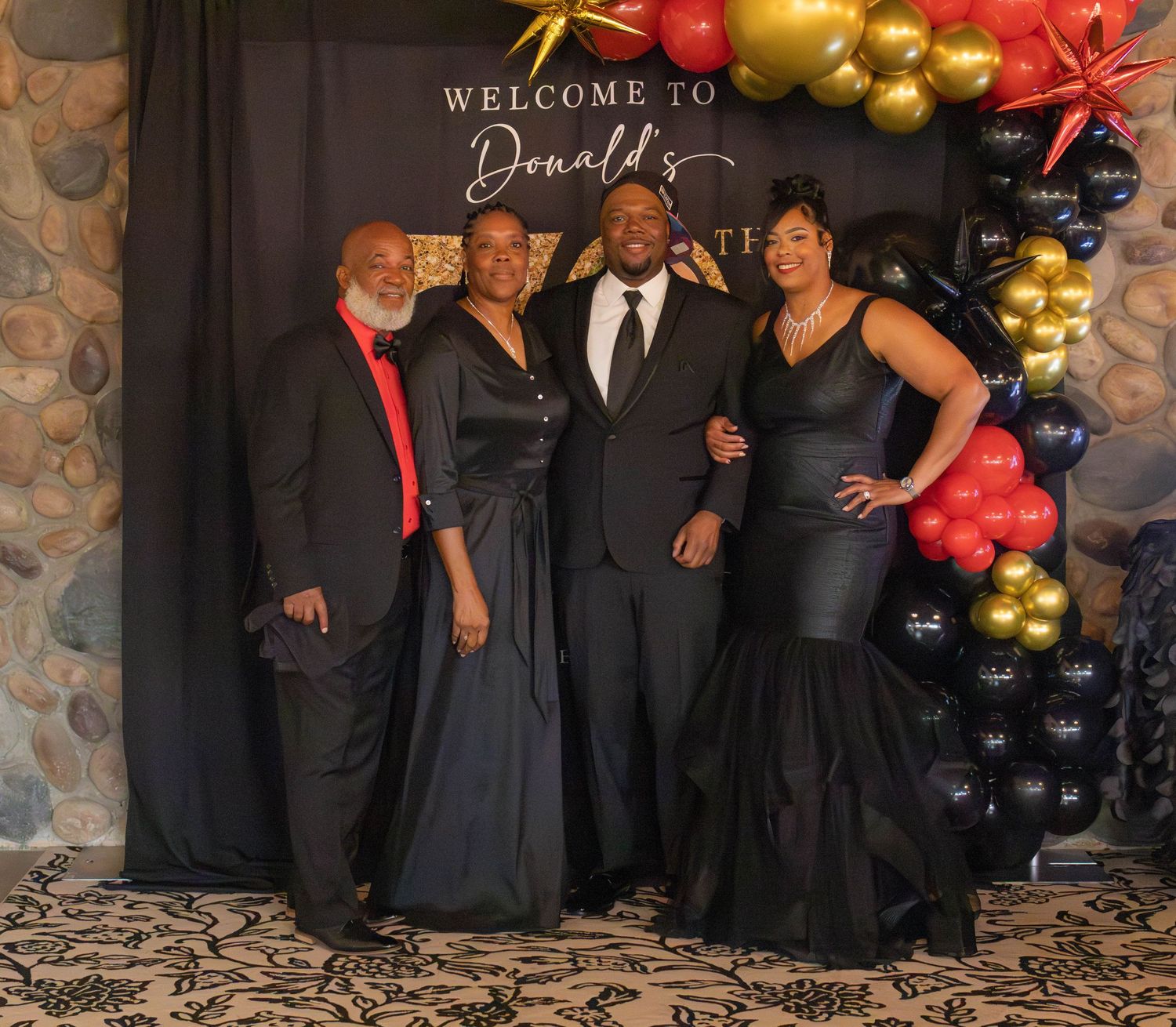 A group poses together at a formal event with black and red balloon decorations against a dark backdrop.
