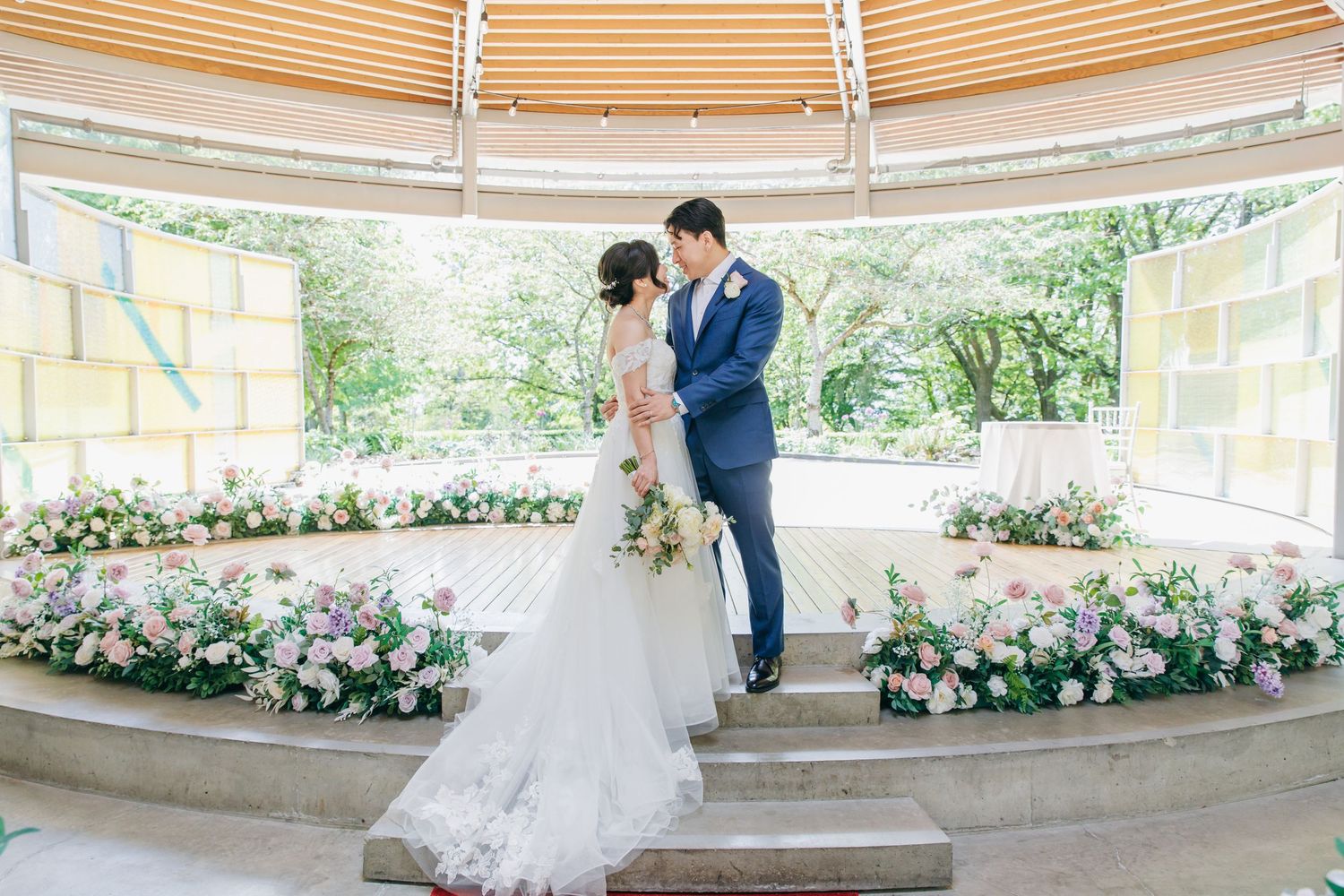 Wedding ceremony setup in a curved pavilion decorated with lush floral arrangements.