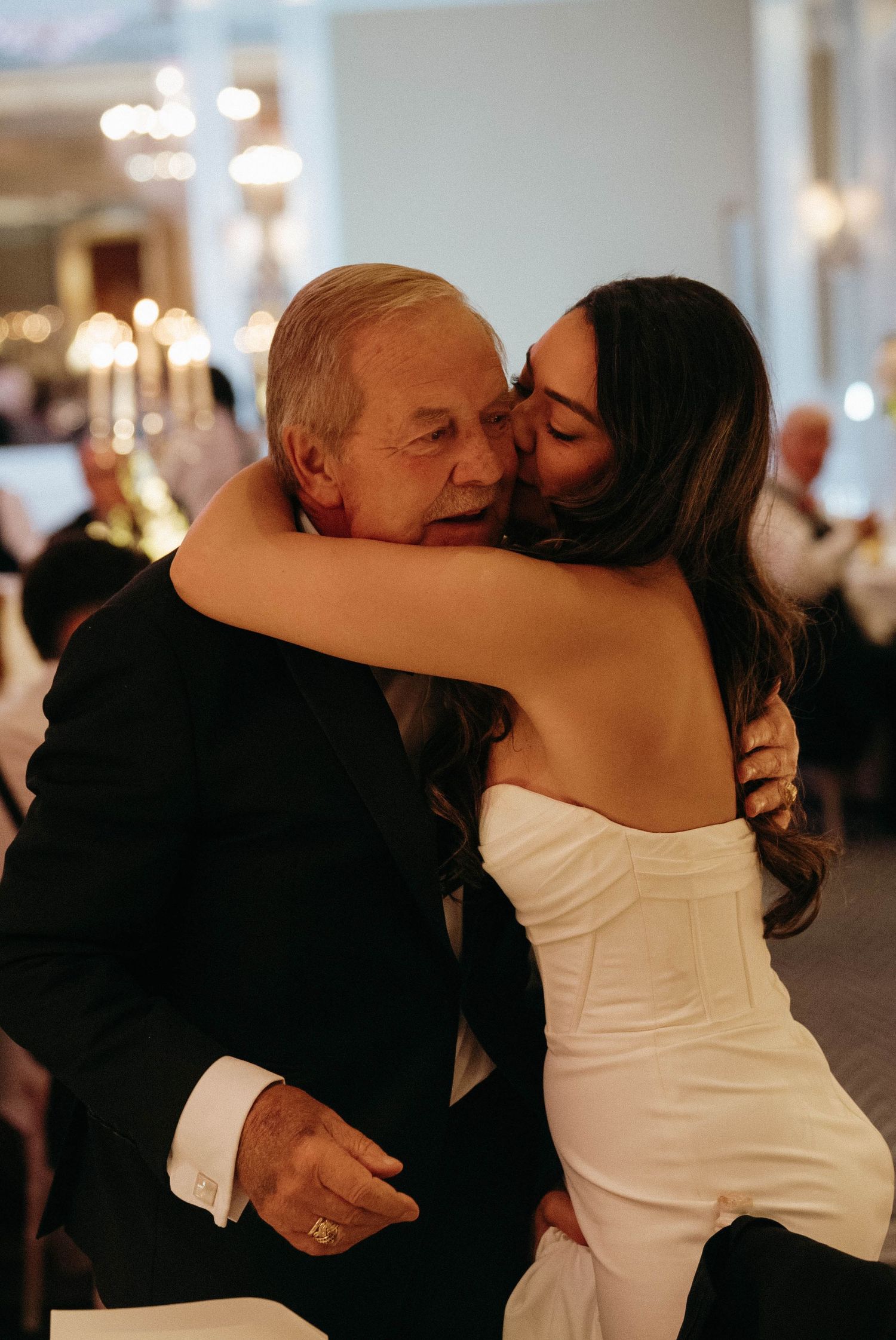 An emotional embrace at a wedding reception with warm lighting and tender expression.