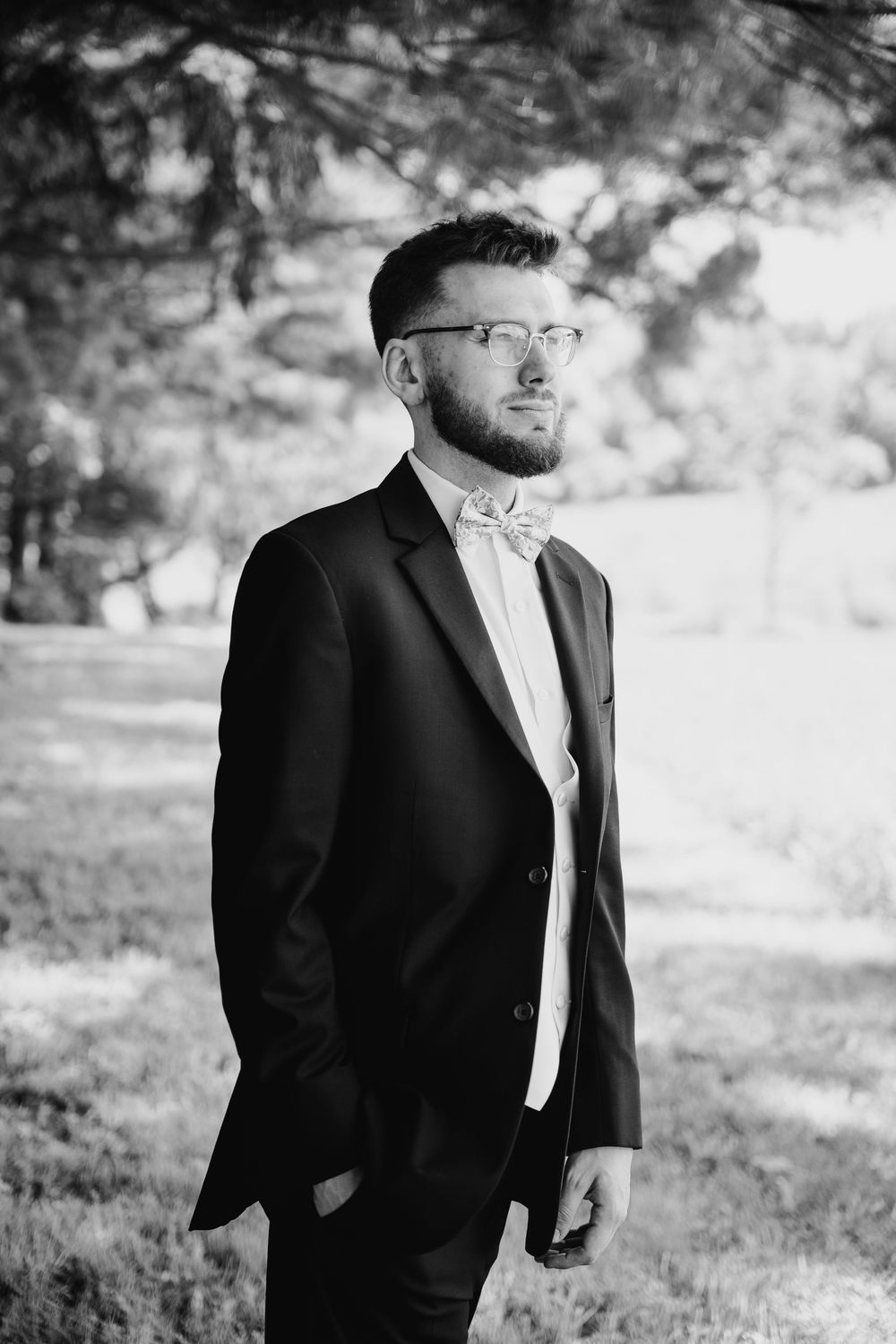 Black and white artistic wedding portrait series showing groom in classic tuxedo and bowtie in outdoor garden setting.