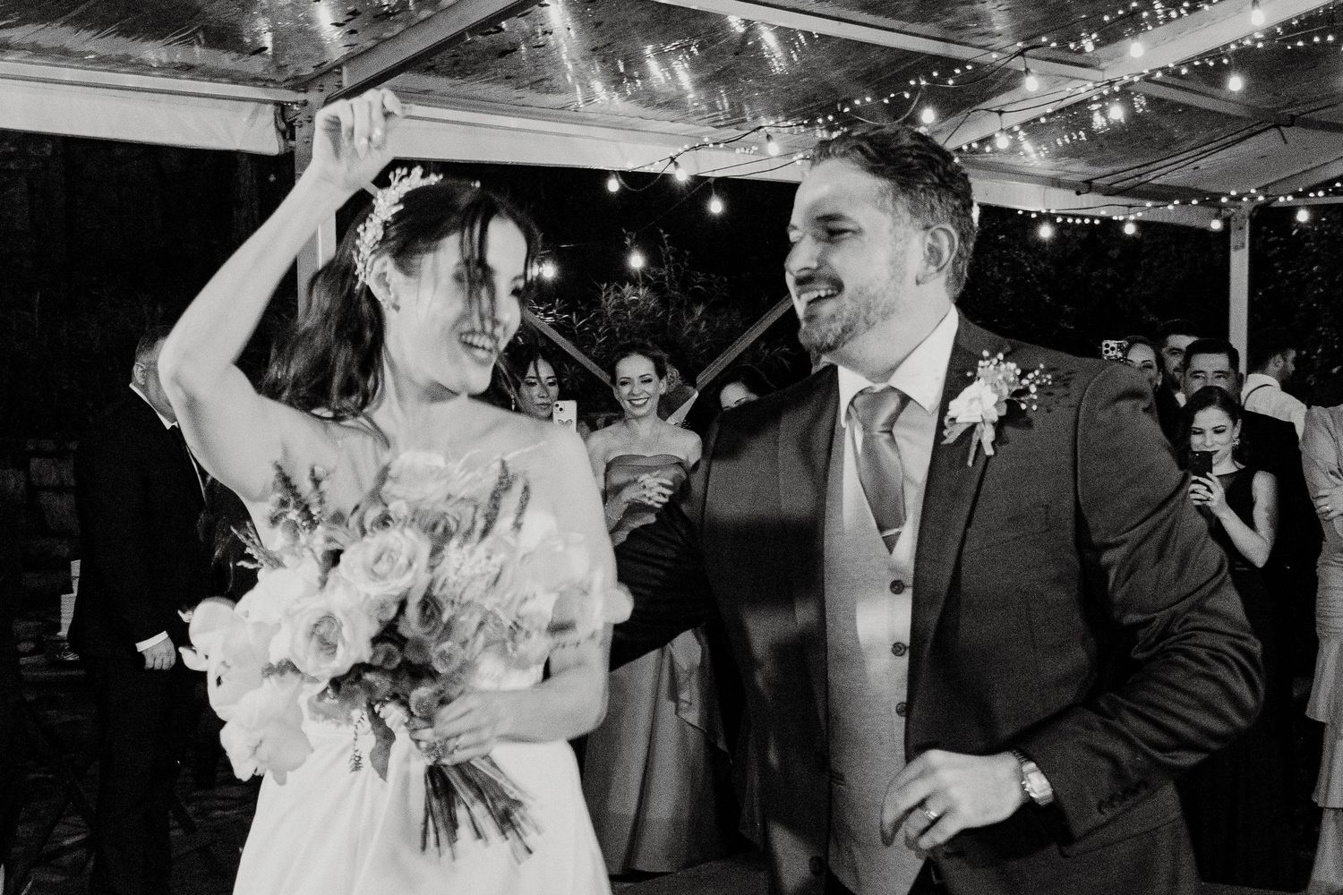 Newlyweds share a joyful dance moment under twinkling lights at their wedding reception.