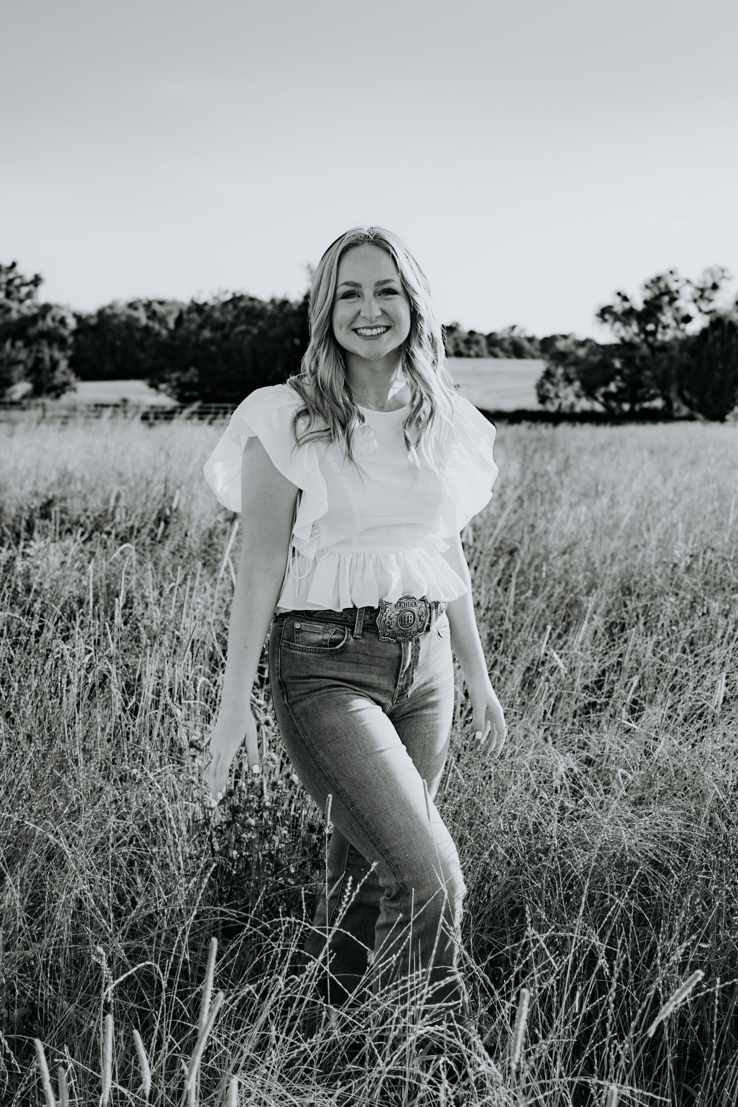 Black and white portrait series in tall grass captures a soft, romantic summertime mood as the subject sits in a field.