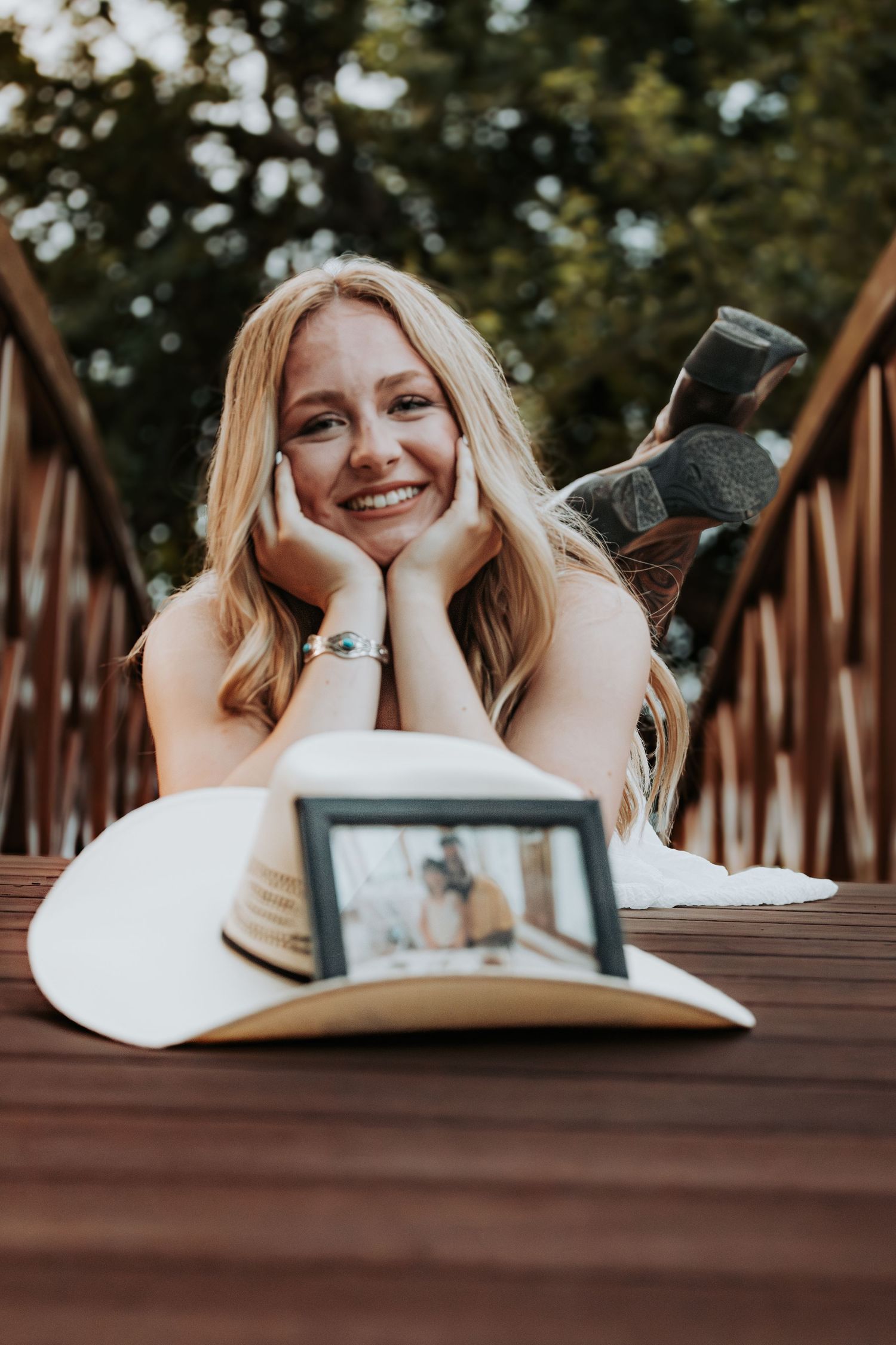 A person lies on a wooden deck outdoors with books and papers while studying in a relaxed pose.