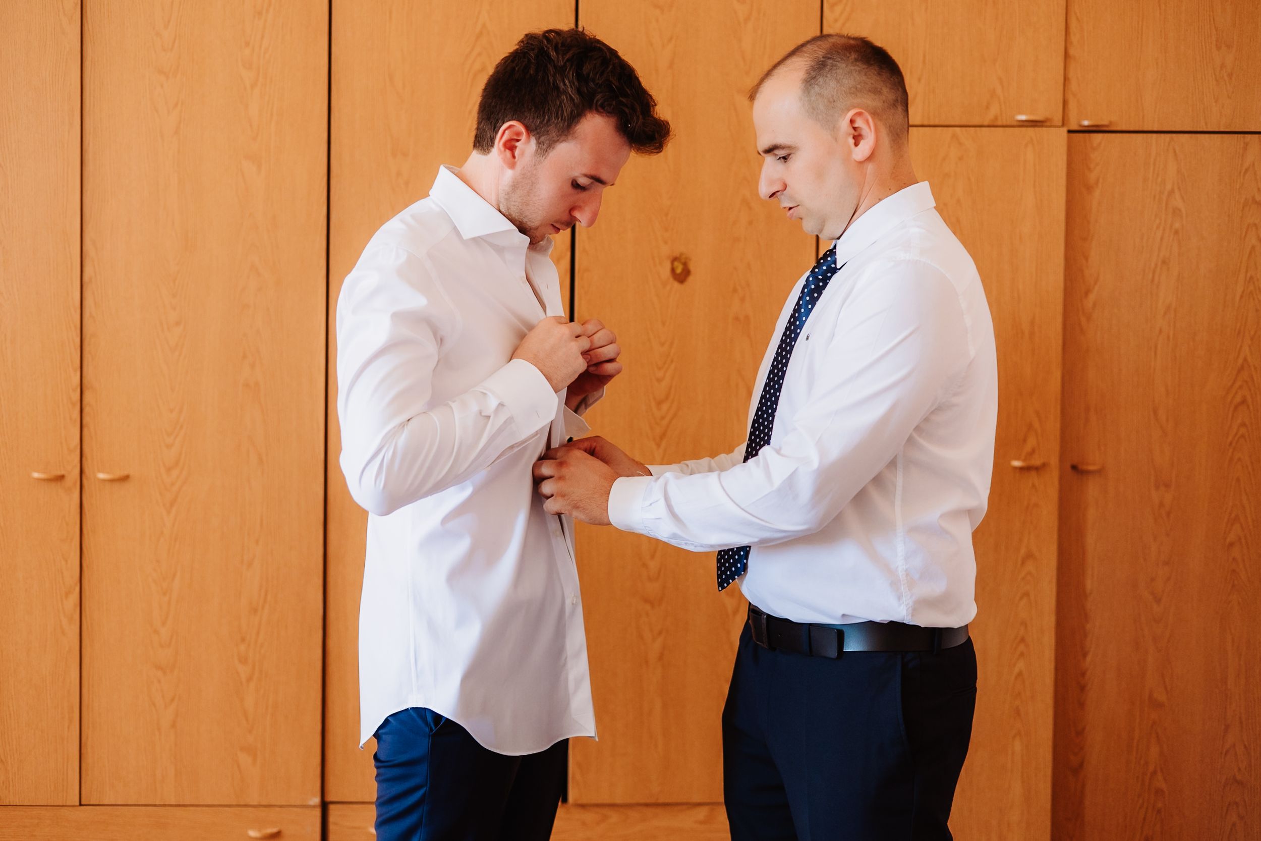 Two professional men in business attire having a close conversation in a hallway with wooden walls.