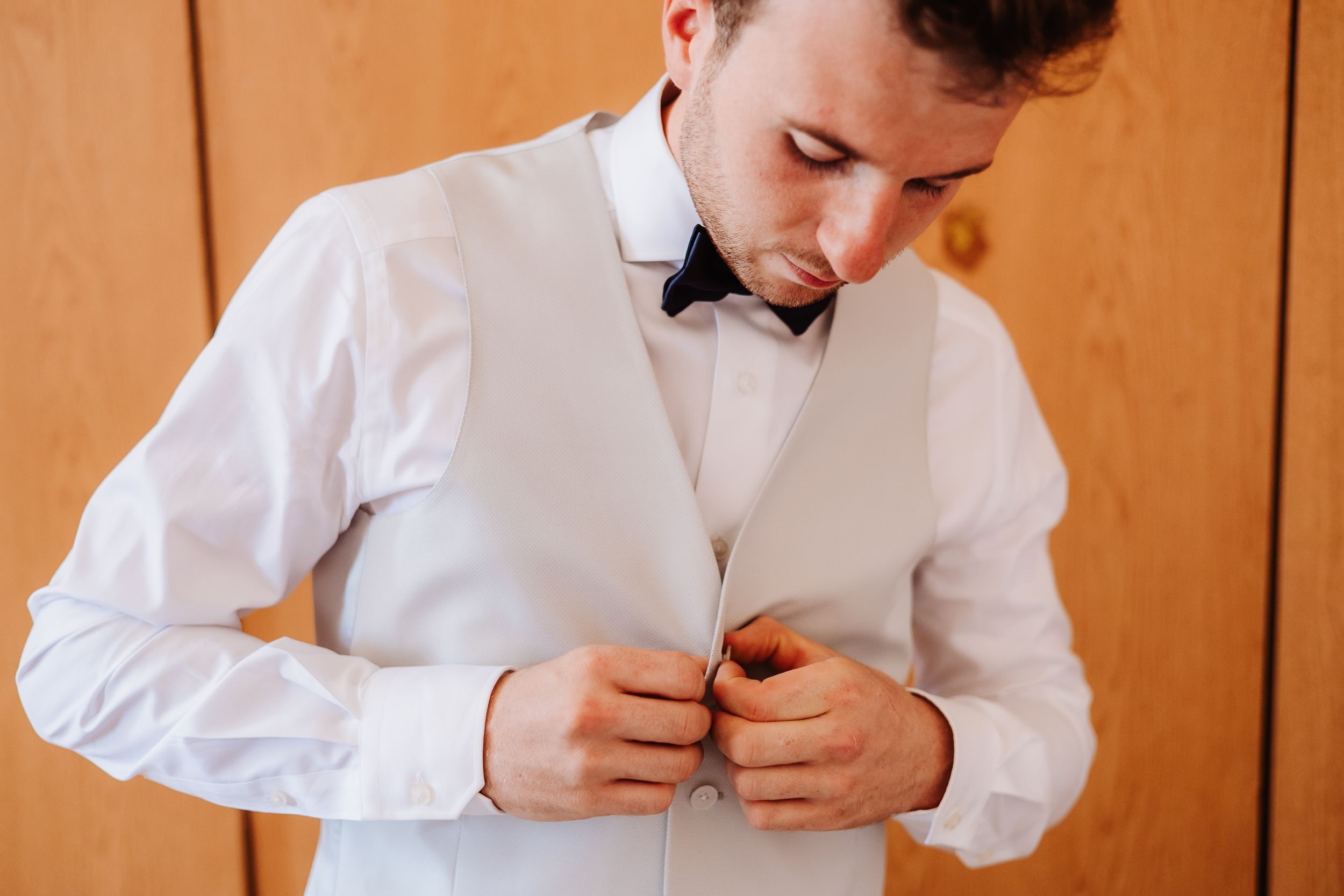 Pair of hands pinning a white button up shirt collar in close-up detail.