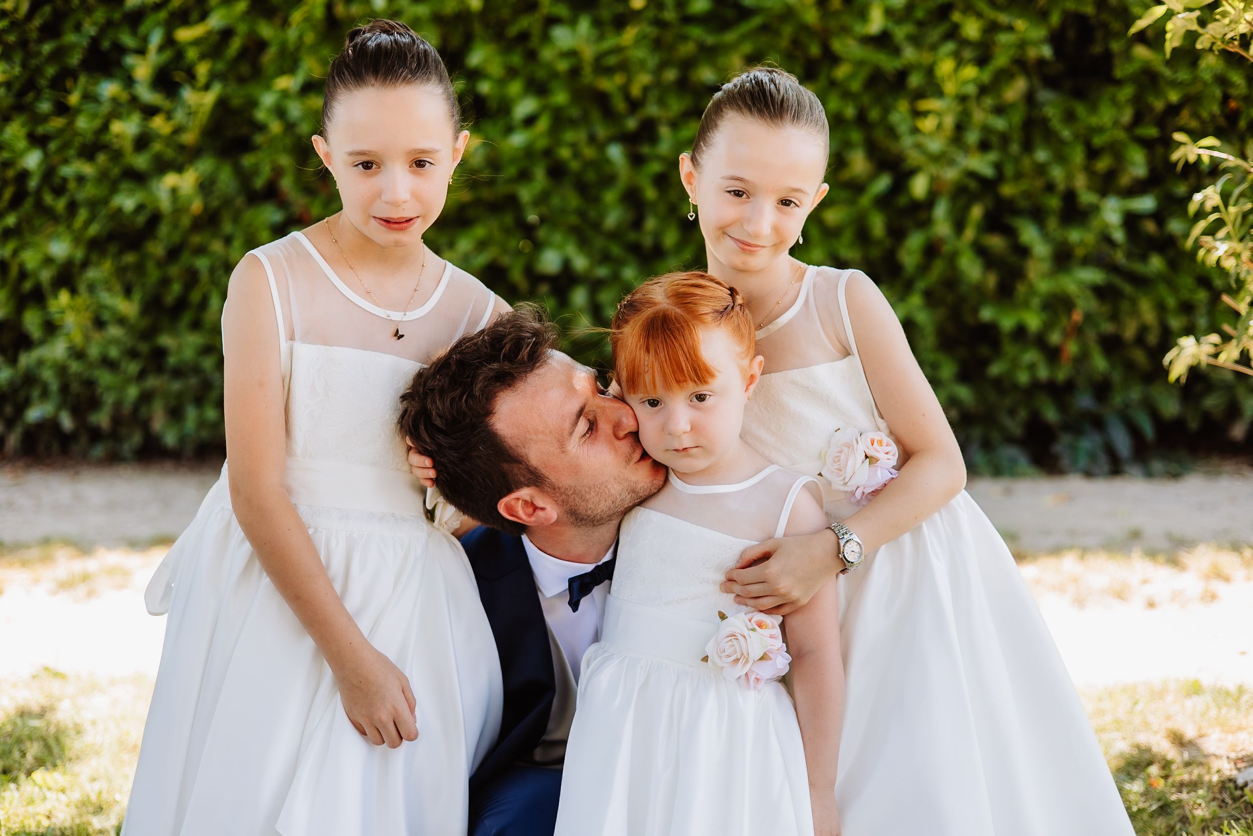 A joyful outdoor moment in white dresses on a sunny day against a green hedge background.