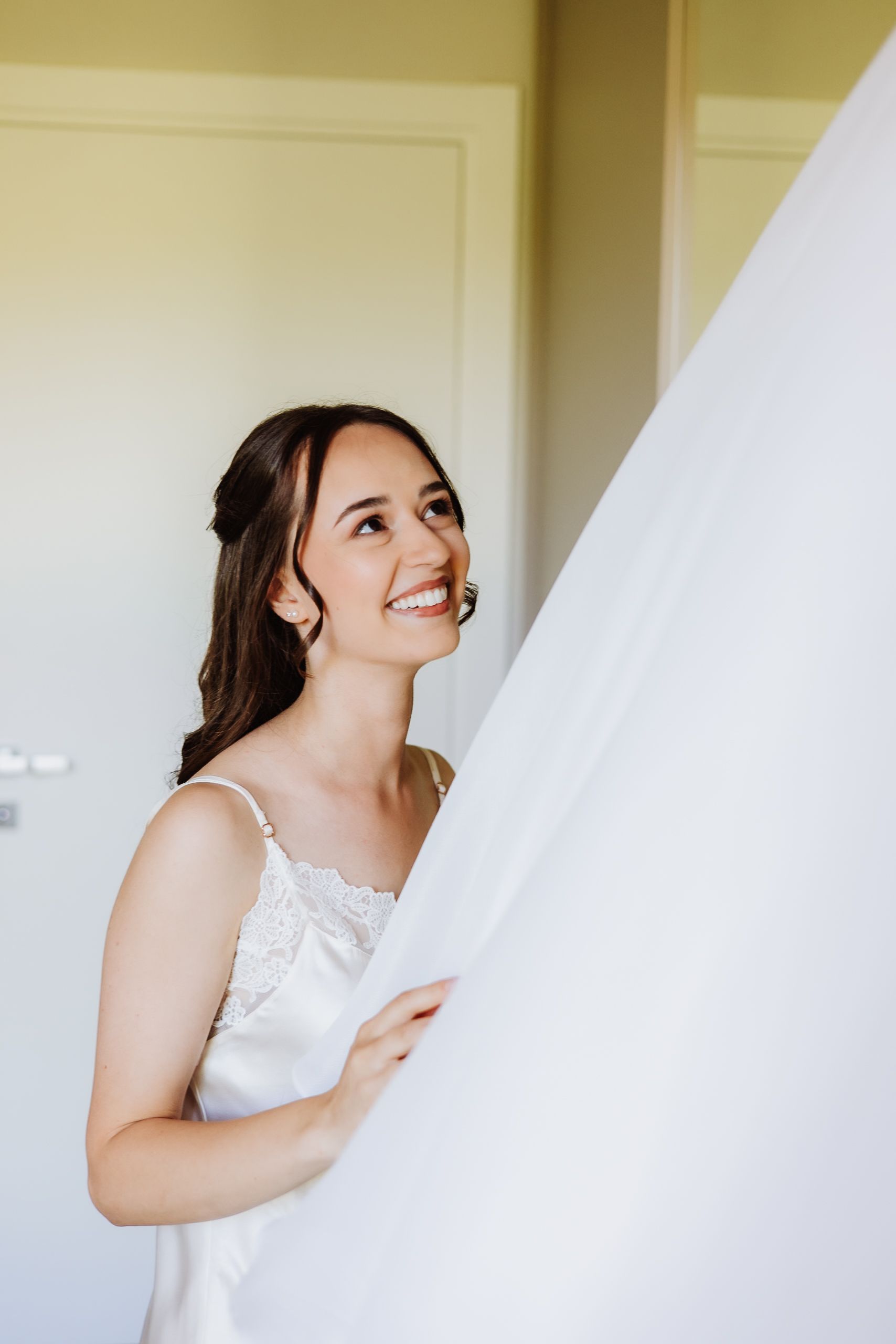 Candid wedding preparation shots showing a bride in a white dress glancing upward with a joyful expression.