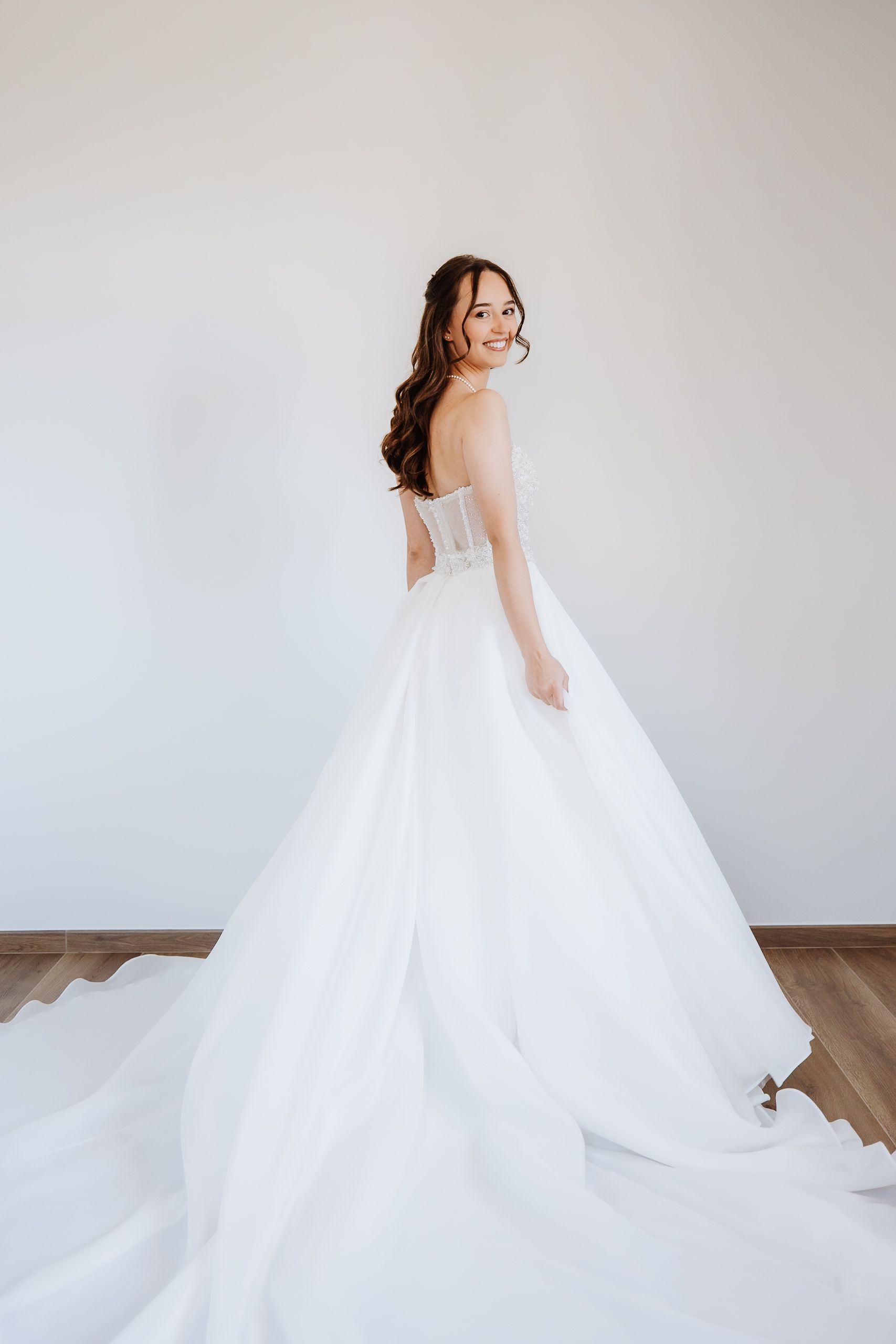 A bride in a flowing white ballgown wedding dress twirls elegantly against a light neutral backdrop, showing off the gown's movement.