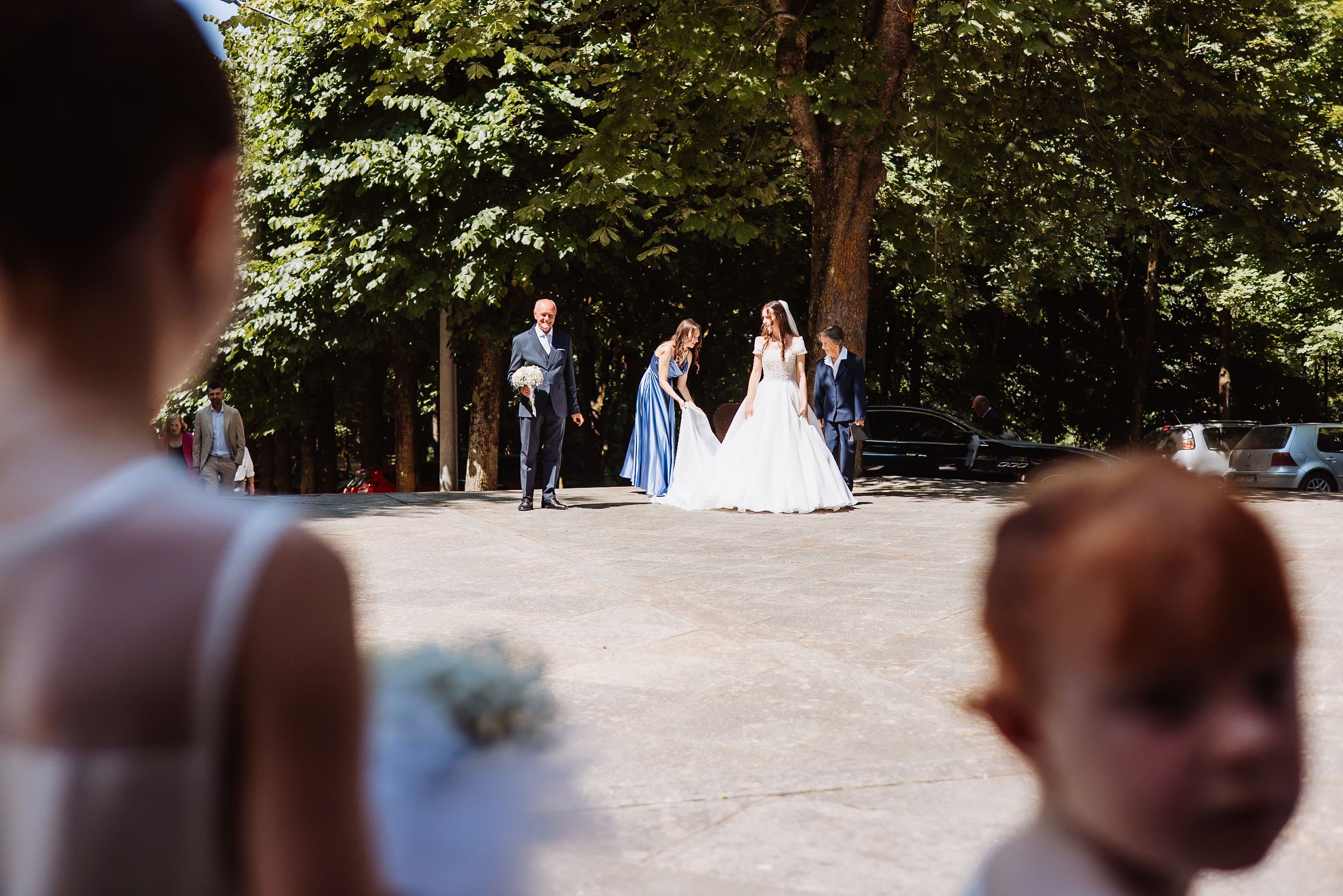 Wedding party joyfully celebrates on a tree-lined outdoor path during summer festivities.