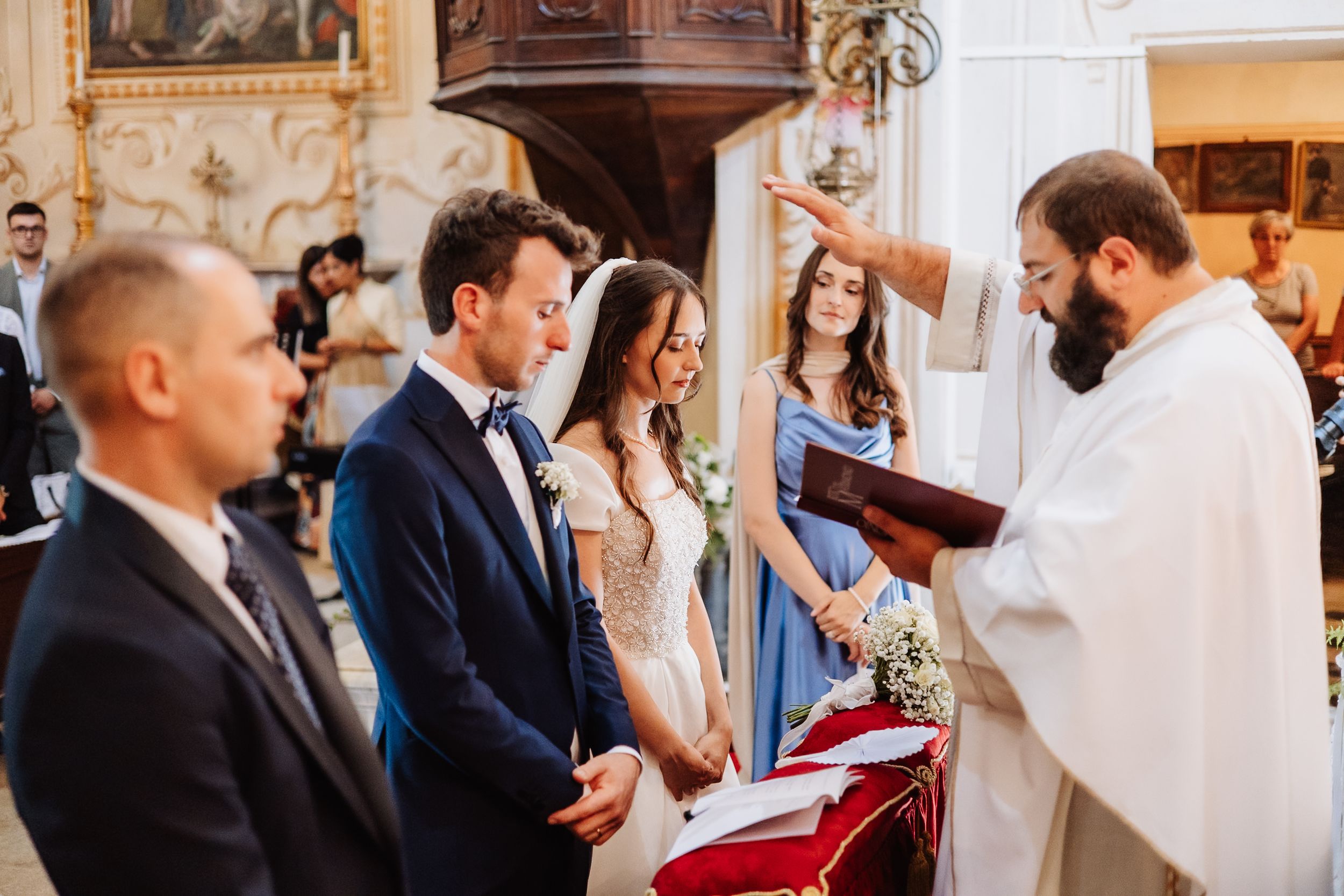 Wedding guests gathered in a traditional church for a ceremony, with rows of people standing in formal attire.