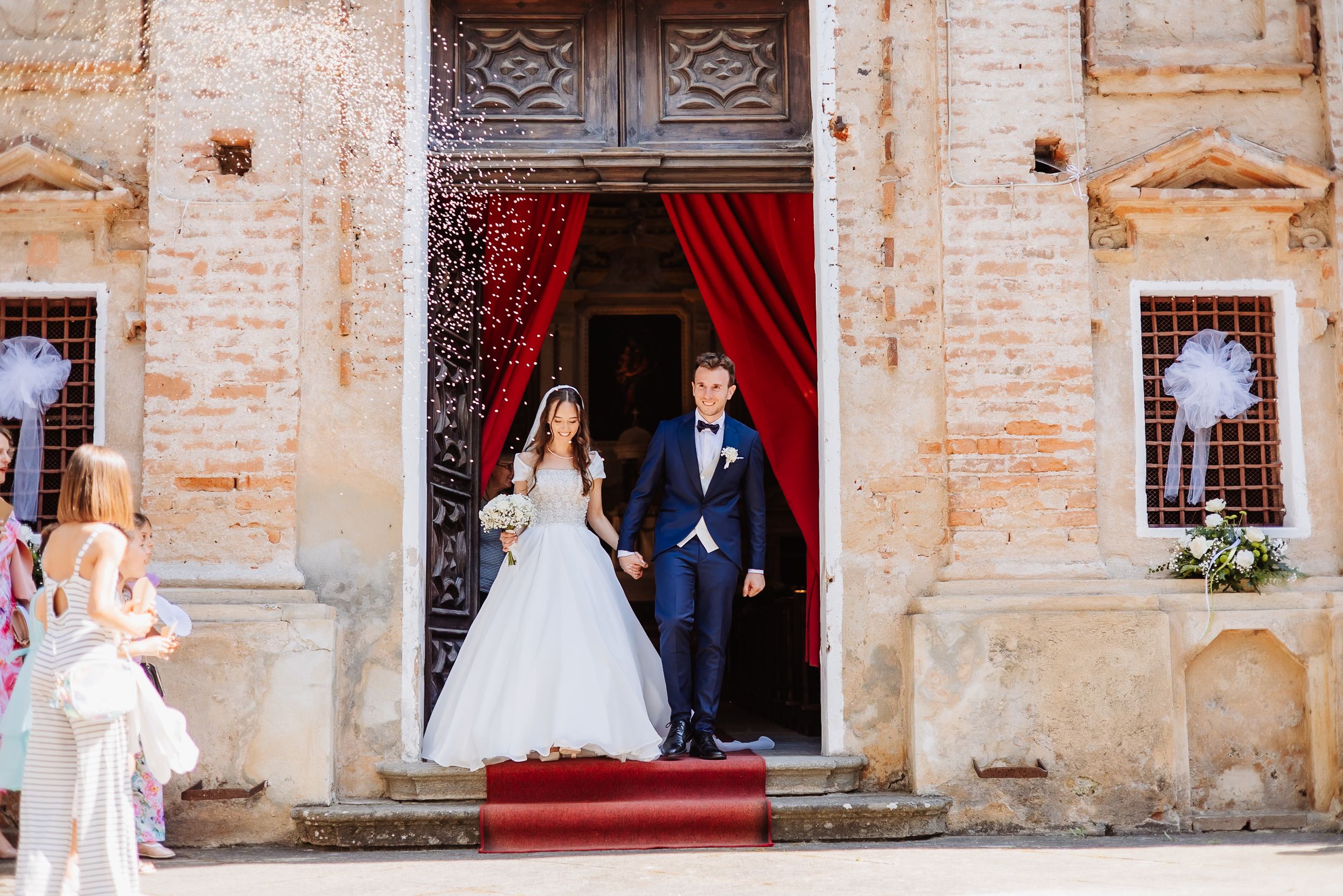 A wedding party portrait set against rustic brick architecture with red carpeting and elegant formal attire.