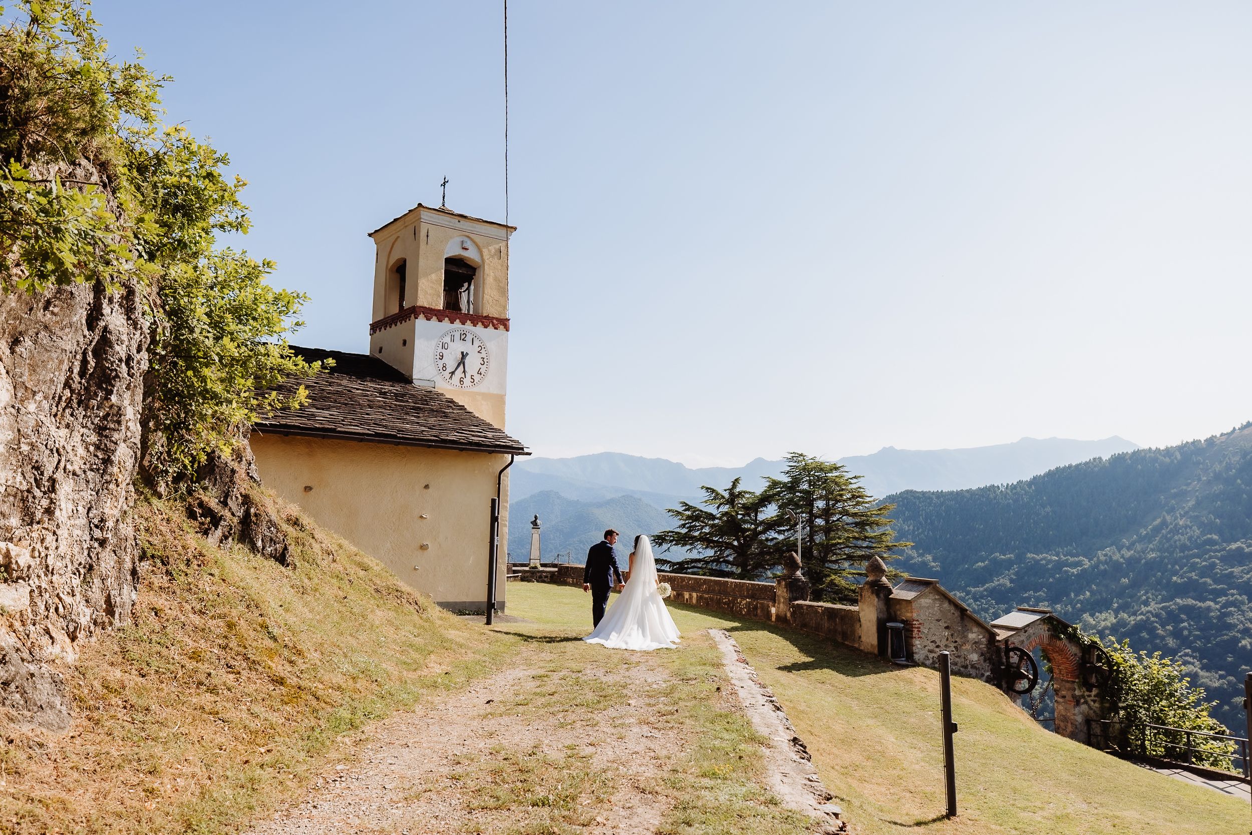 Mountain path leading to a historic church bell tower perched on a hilltop in a scenic rural landscape.