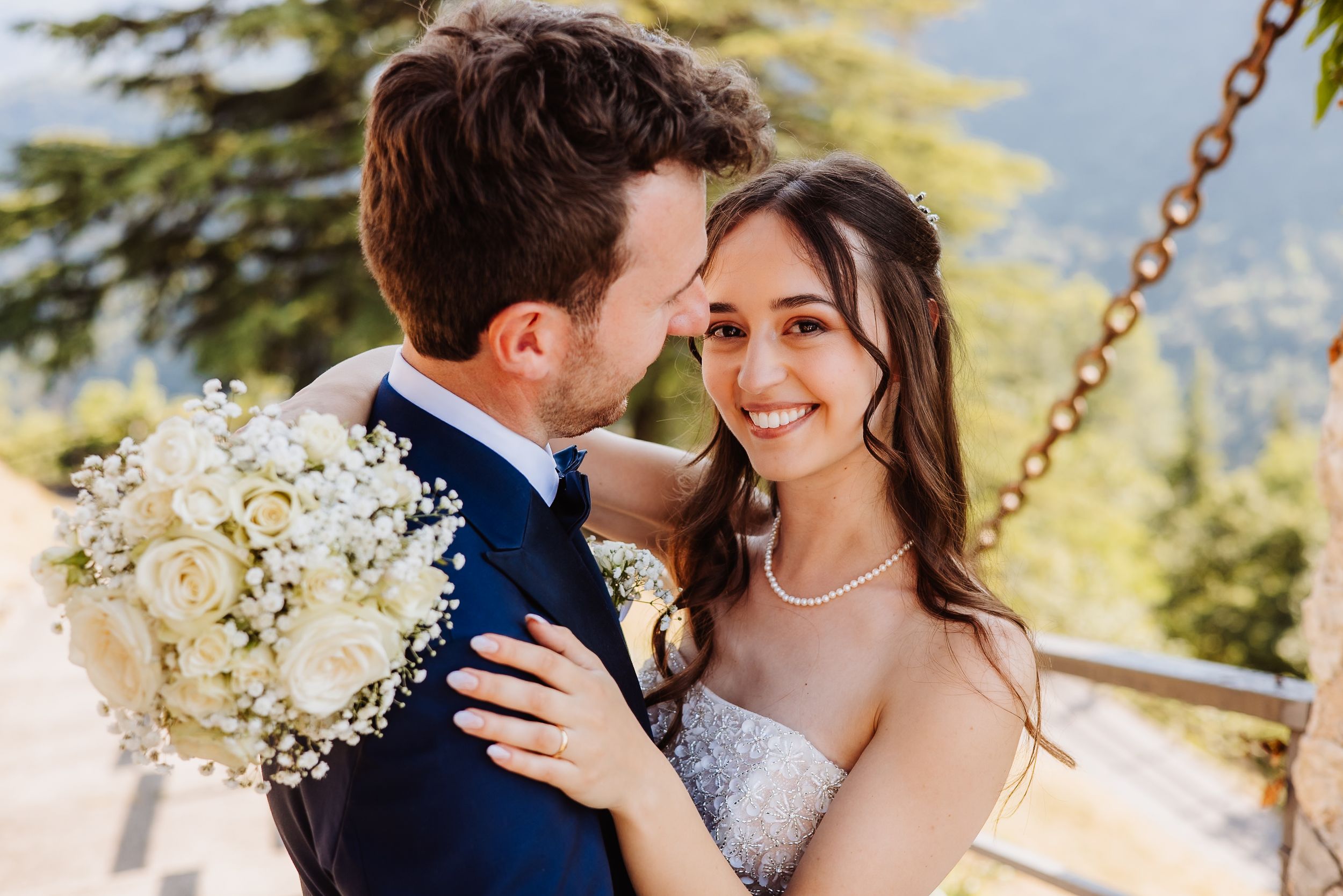 A couple embraces in front of rugged mountain peaks and evergreen trees on their wedding day.