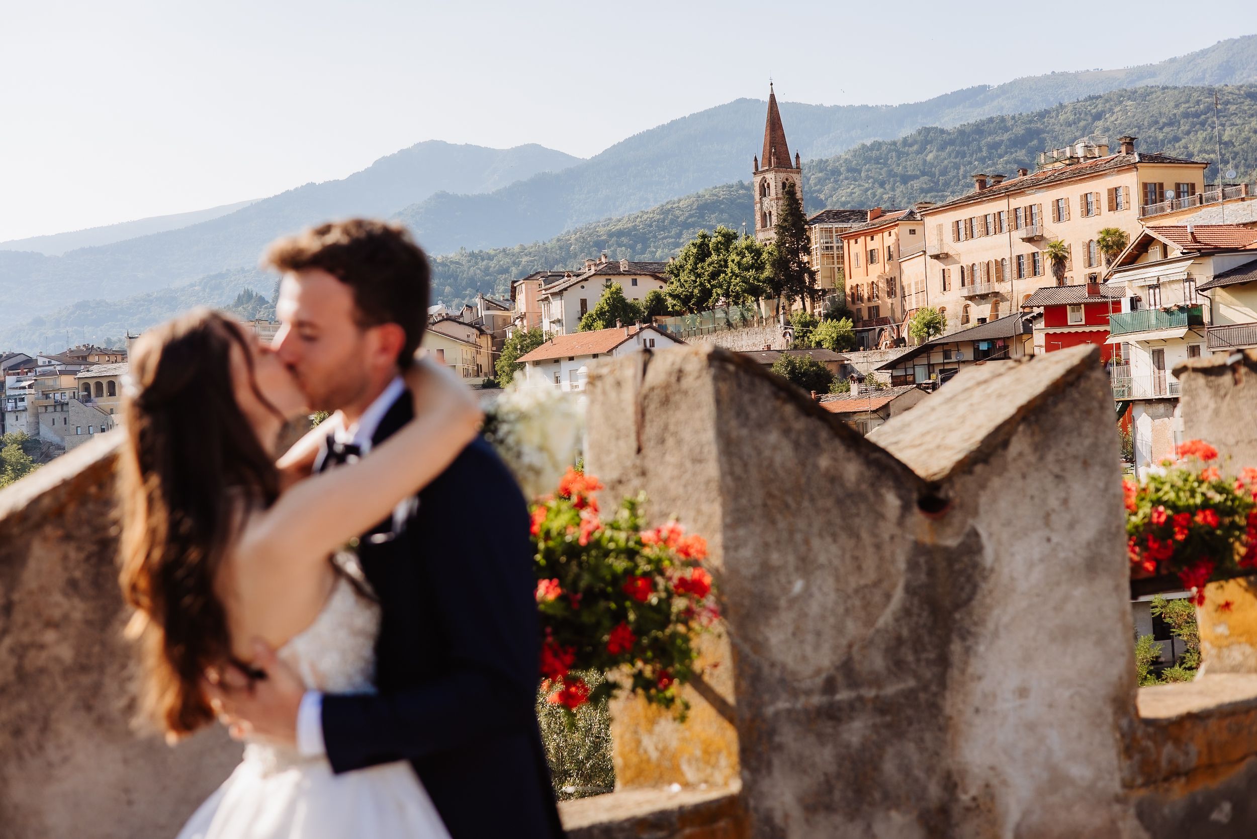 Couple embracing and kissing on a rooftop terrace overlooking a Mediterranean mountain landscape and village.