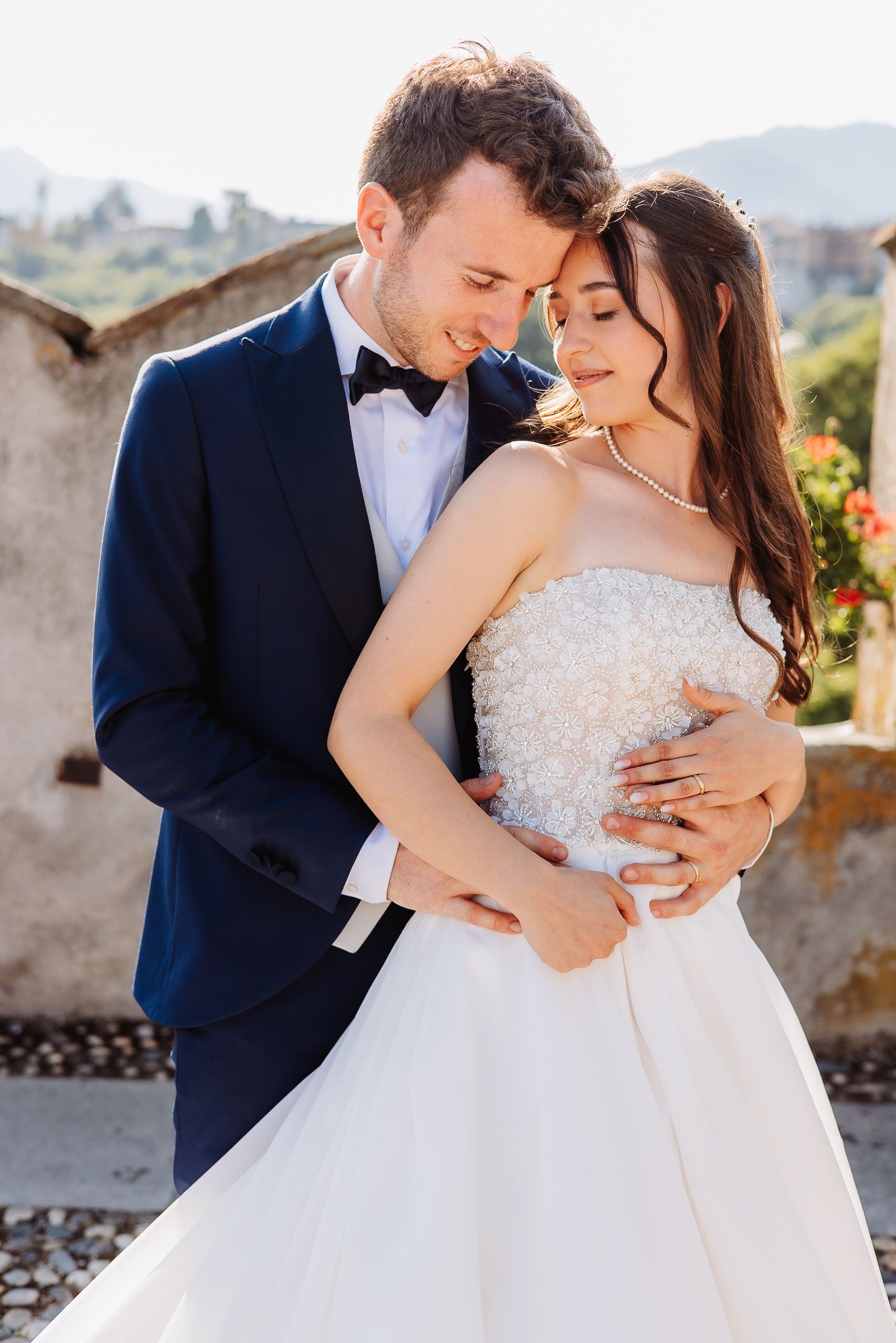Romantic wedding moment captured against stone walls and traditional Italian architecture in warm sunlight.