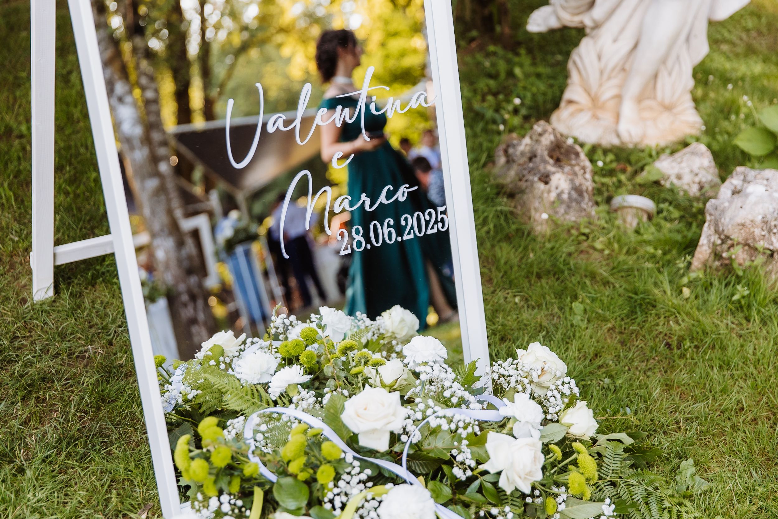 Wedding decorations with white floral arrangements and names displayed on signs at an outdoor ceremony setup.