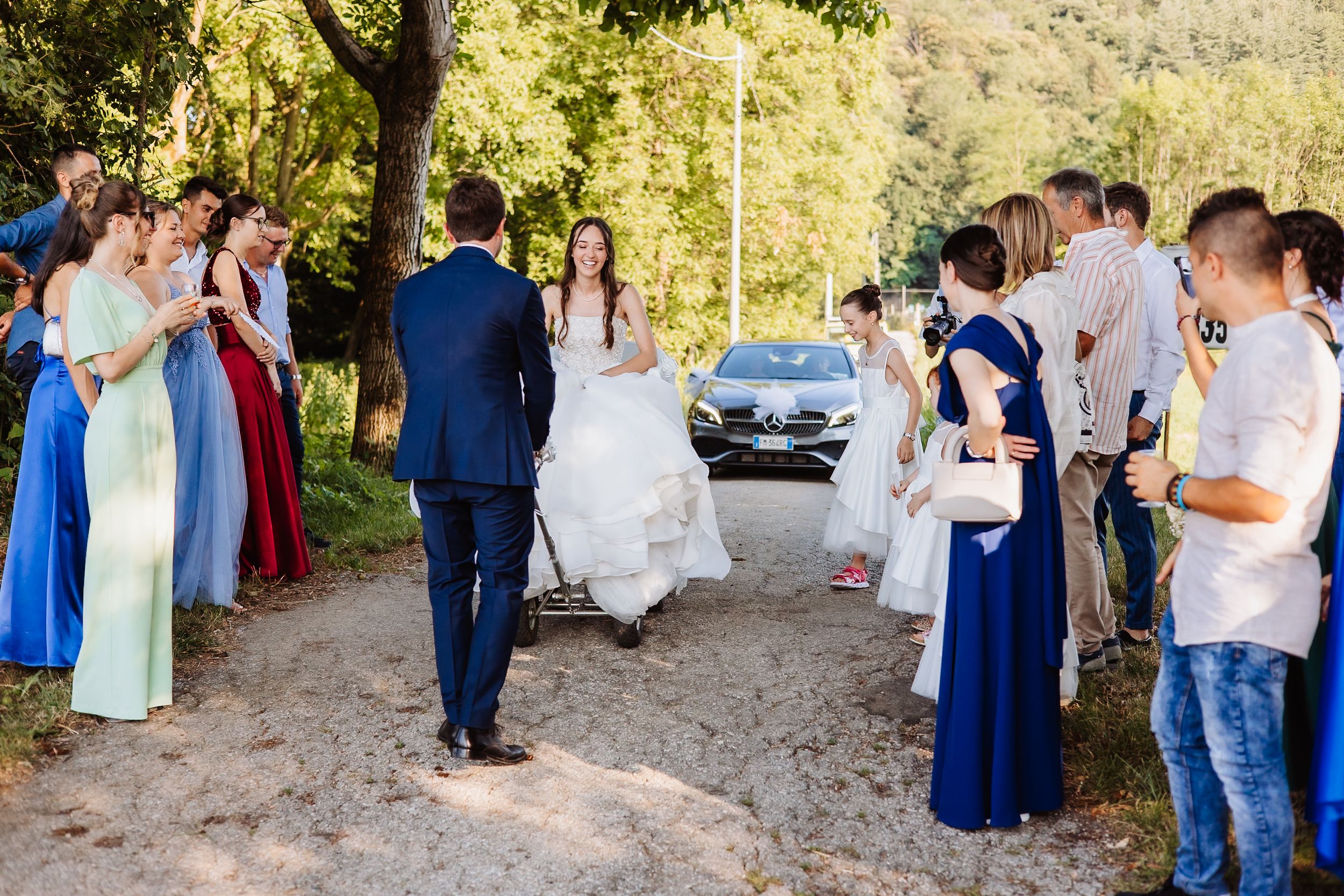 Wedding guests gathered outdoors on a wooded path during a sunny afternoon celebration.