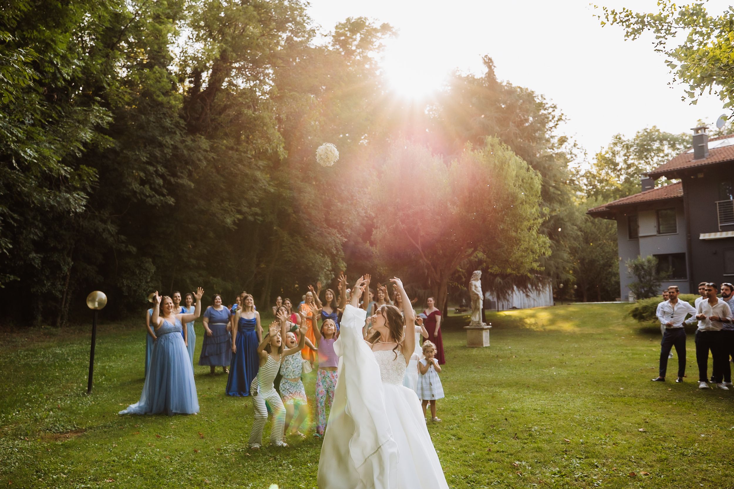 Wedding party group walks through a sunlit meadow at golden hour, with lens flares illuminating the summer evening scene.
