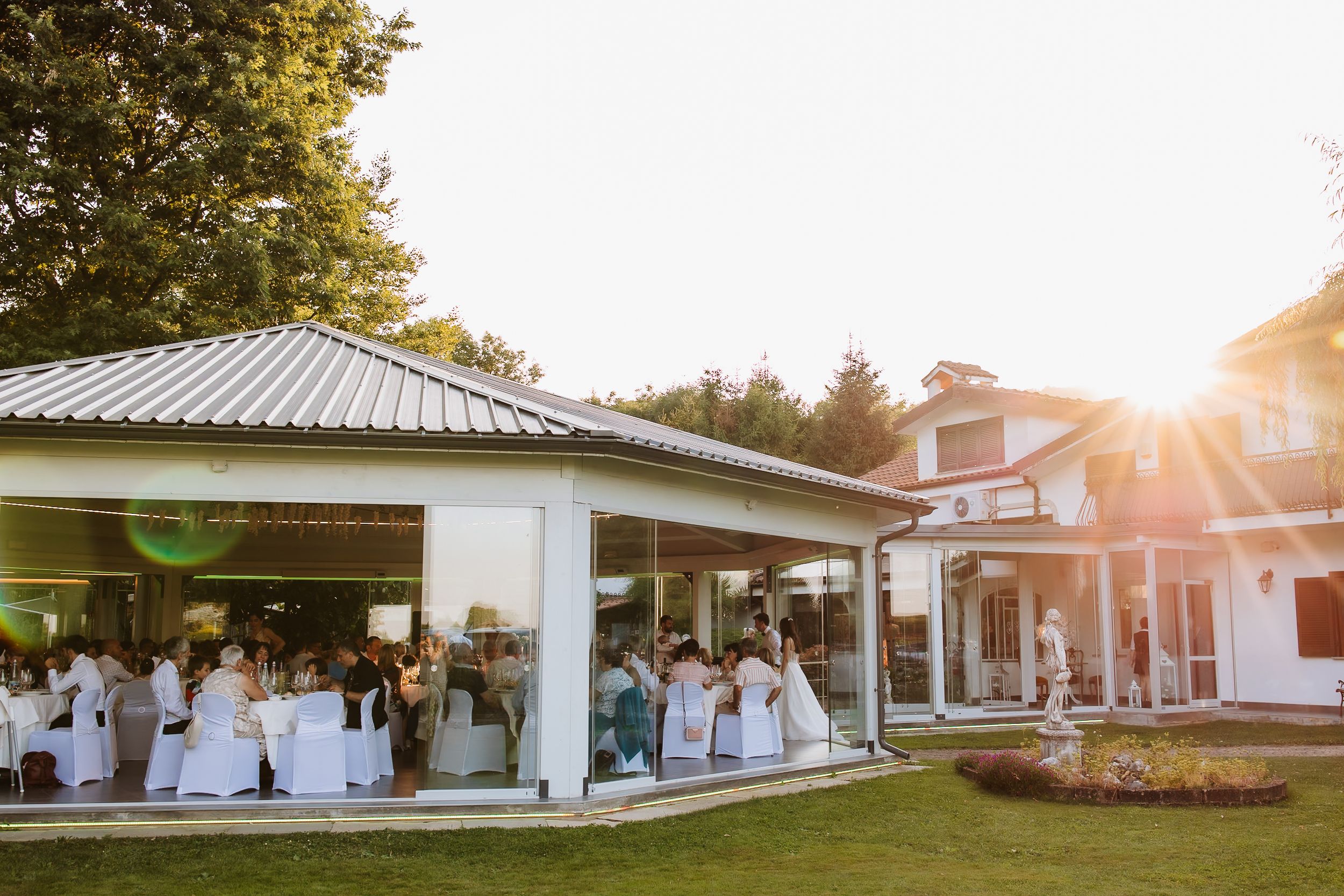 Beautiful outdoor wedding venue layout with white covered seating areas and glowing sunset through the trees.
