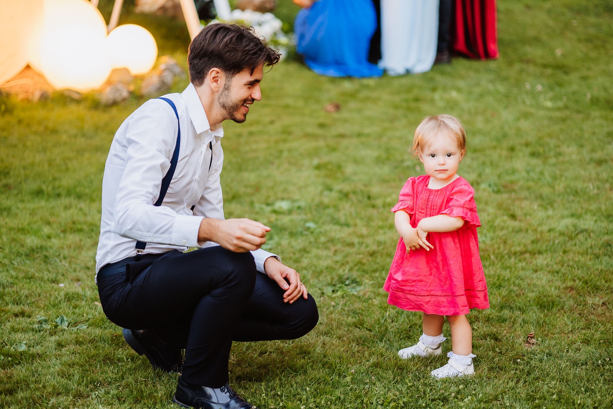 Children in matching red outfits play together on a grassy lawn with adults nearby during outdoor activities.