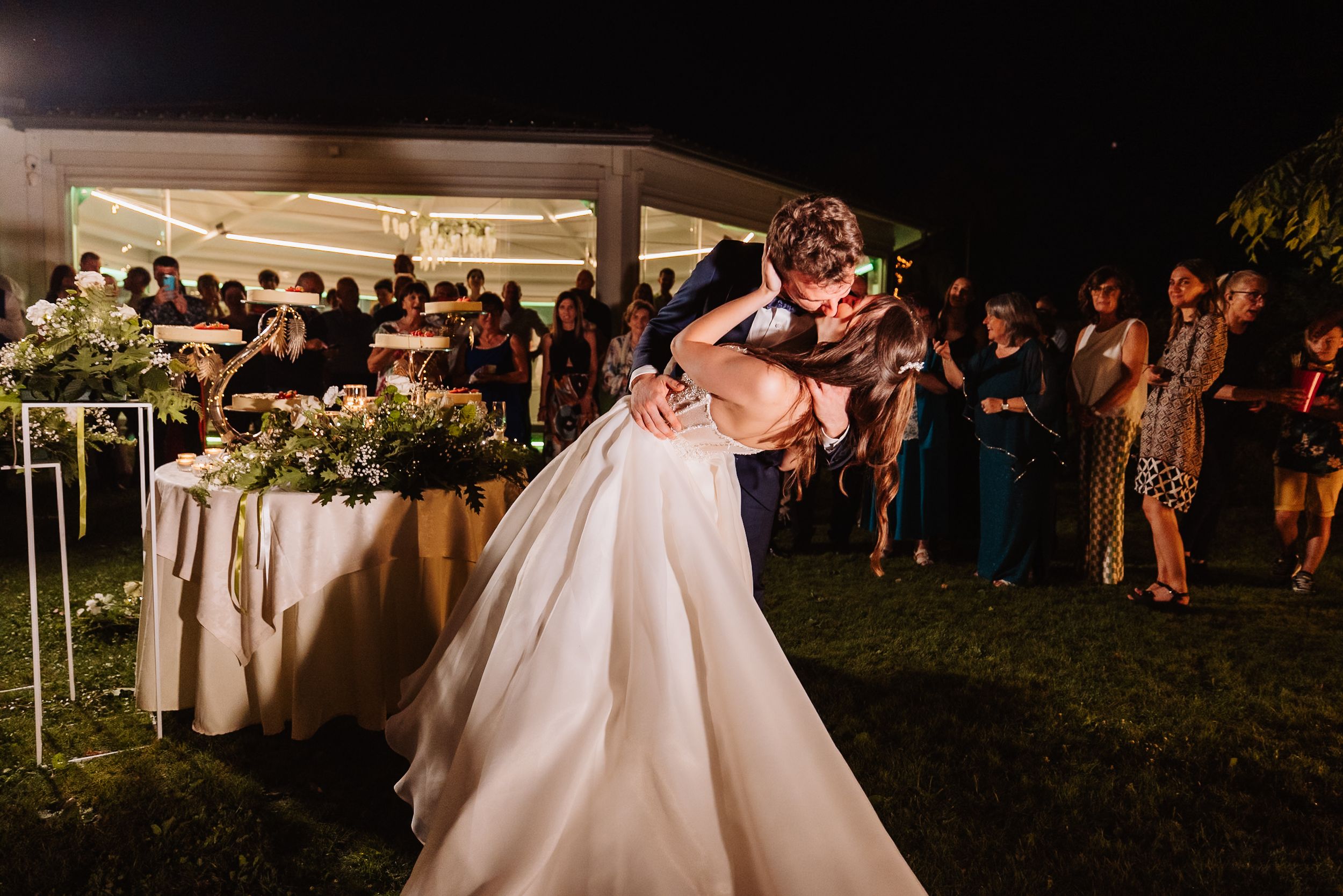 Wedding reception guests enjoying an outdoor evening celebration with glowing lights and floral decorations.