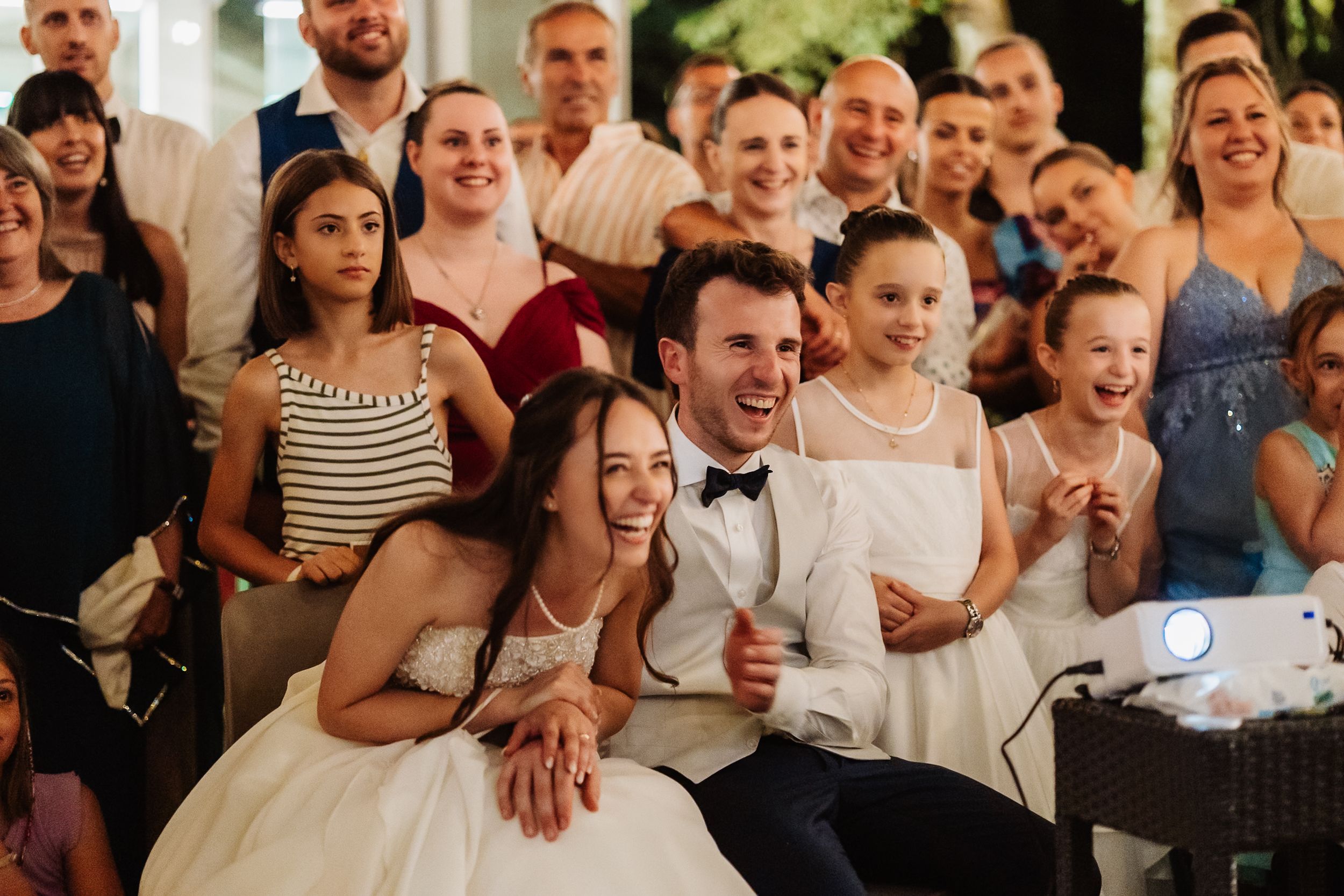 A large group of wedding guests smiling and reacting with joy during a celebration.
