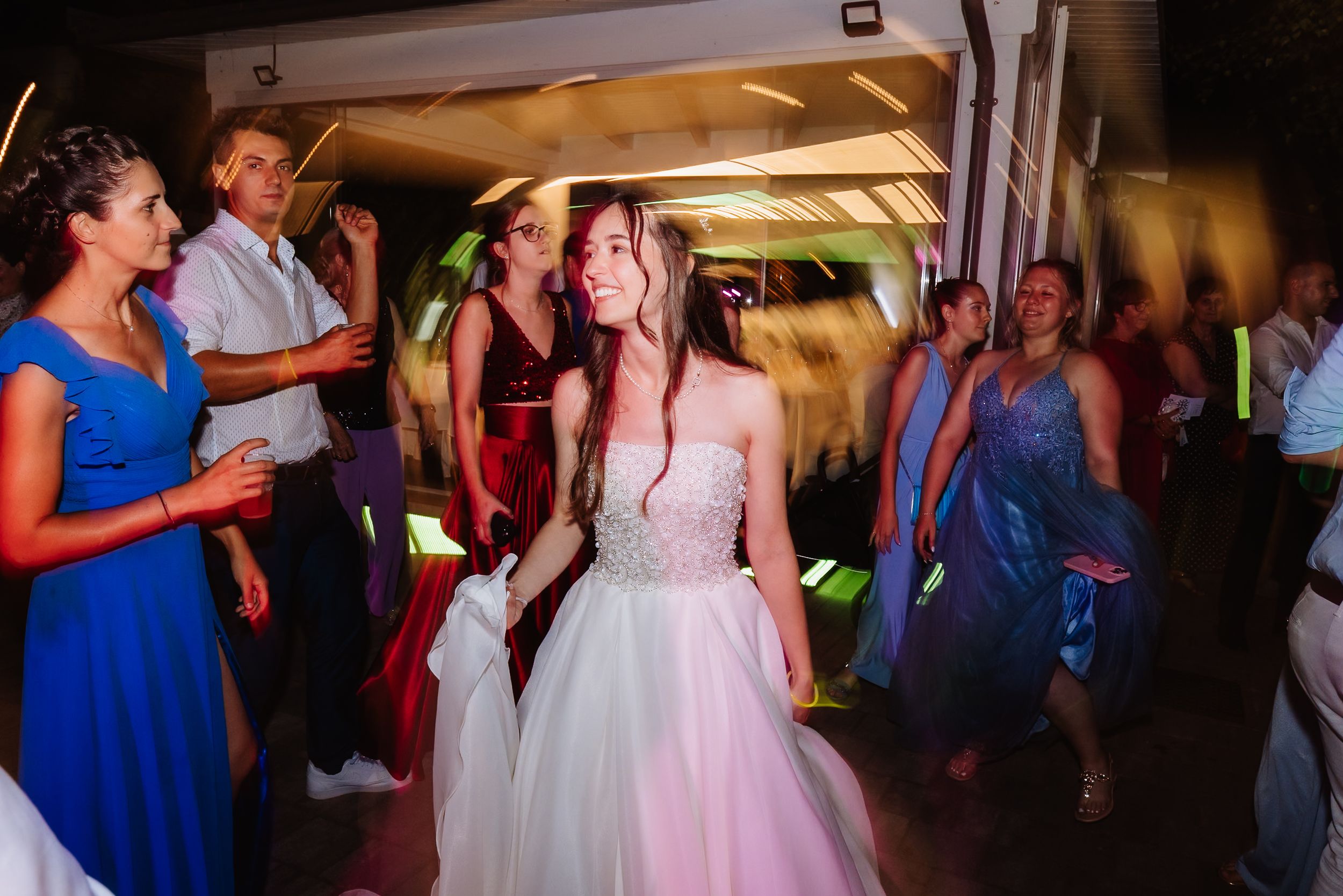People dancing and celebrating during a wedding reception in indoor venue with colorful lighting.
