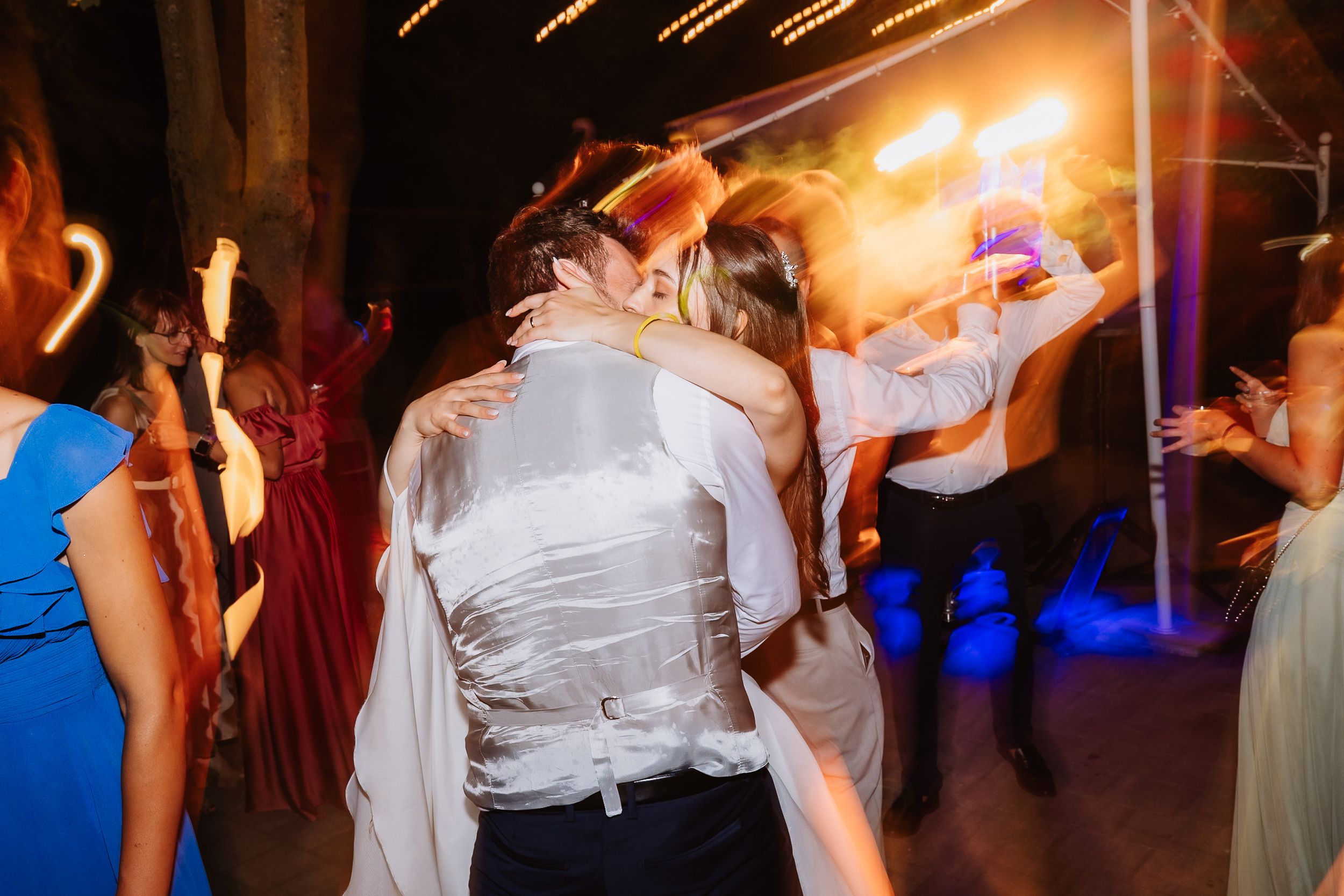 Wedding guests dancing together under warm lighting at a lively evening reception celebration.