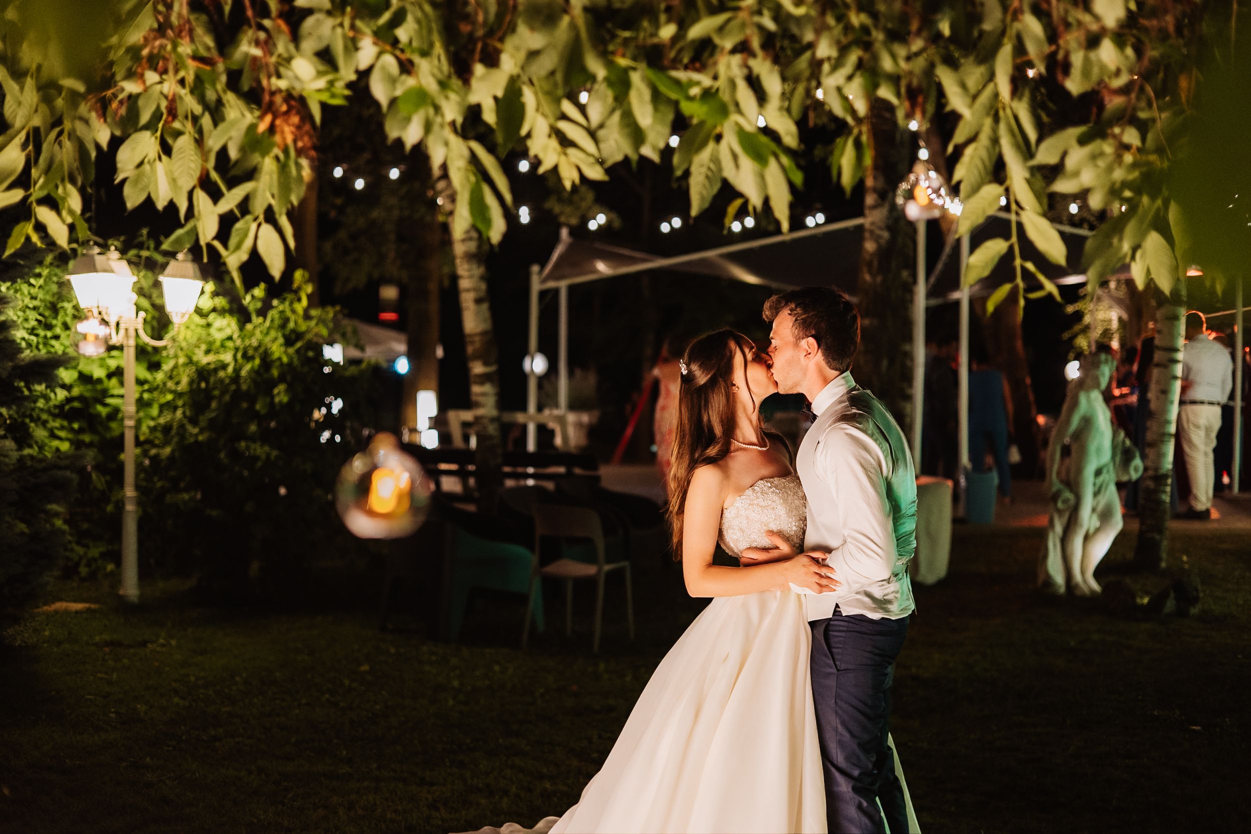 A couple shares their first dance as newlyweds at an evening garden reception with string lights overhead.