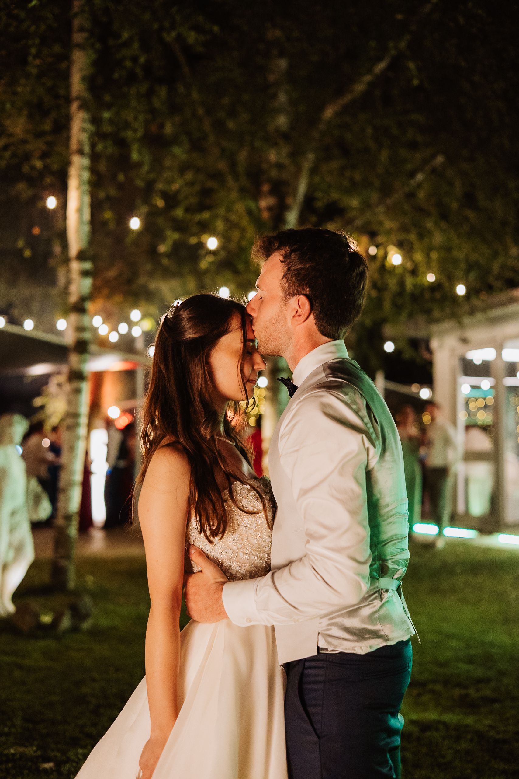 A romantic couple shares an intimate evening dance under string lights in a park at twilight.