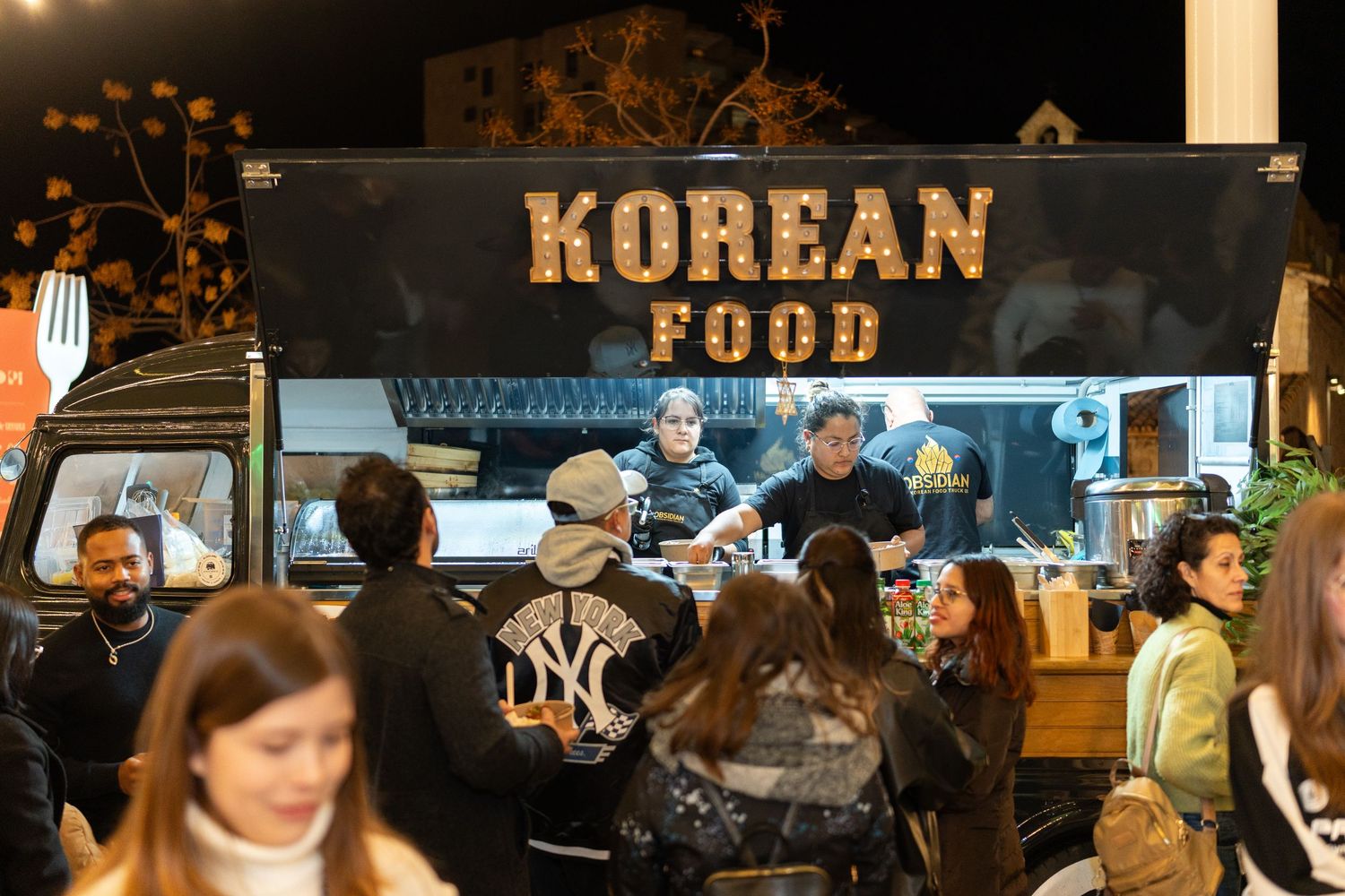 Food truck coreano de noche con clientes esperando sus pedidos, escena urbana ideal para fotografía lifestyle en Mallorca.